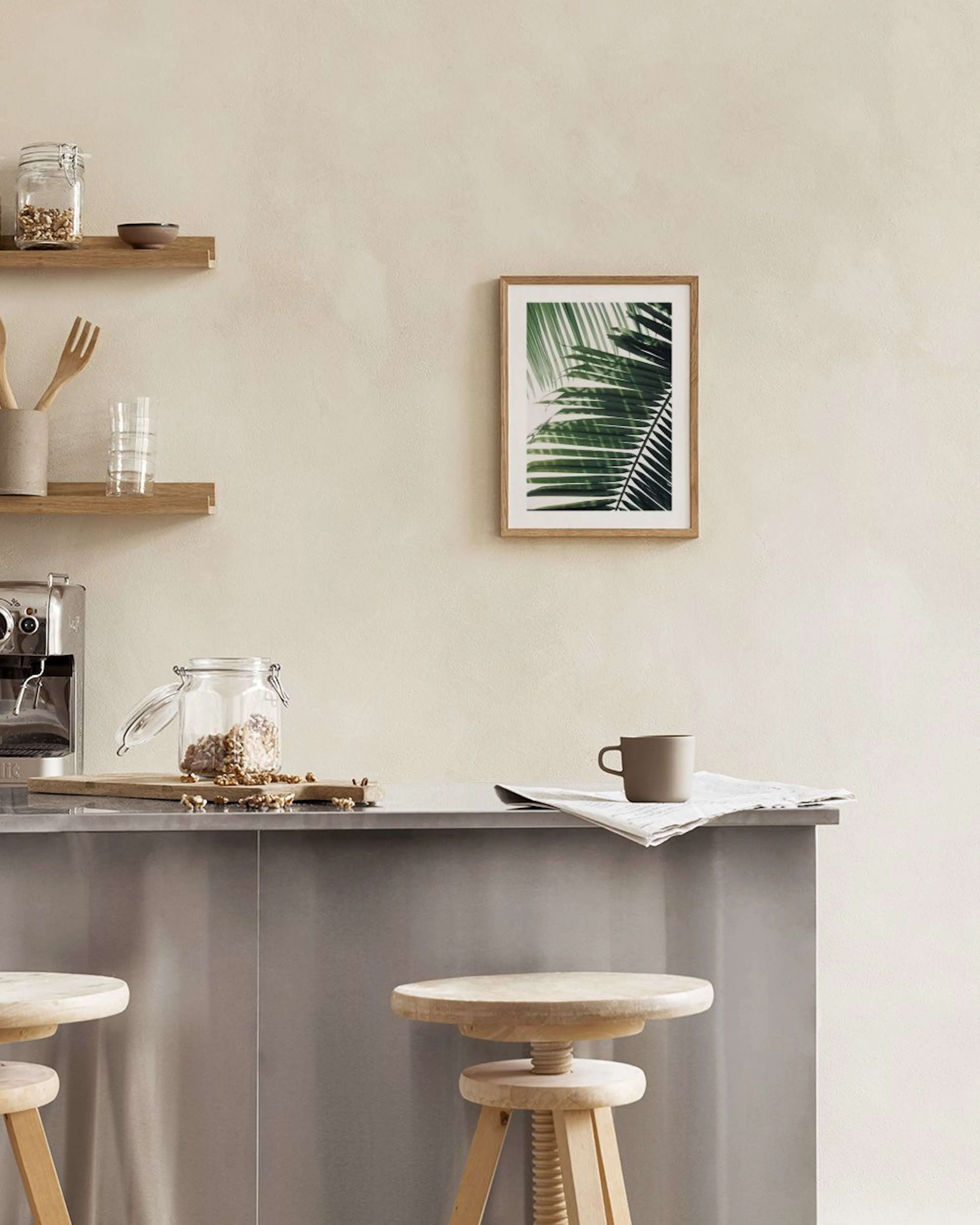 A print of lush green palm leaves hanging above a light wooden table and a white armchair.
