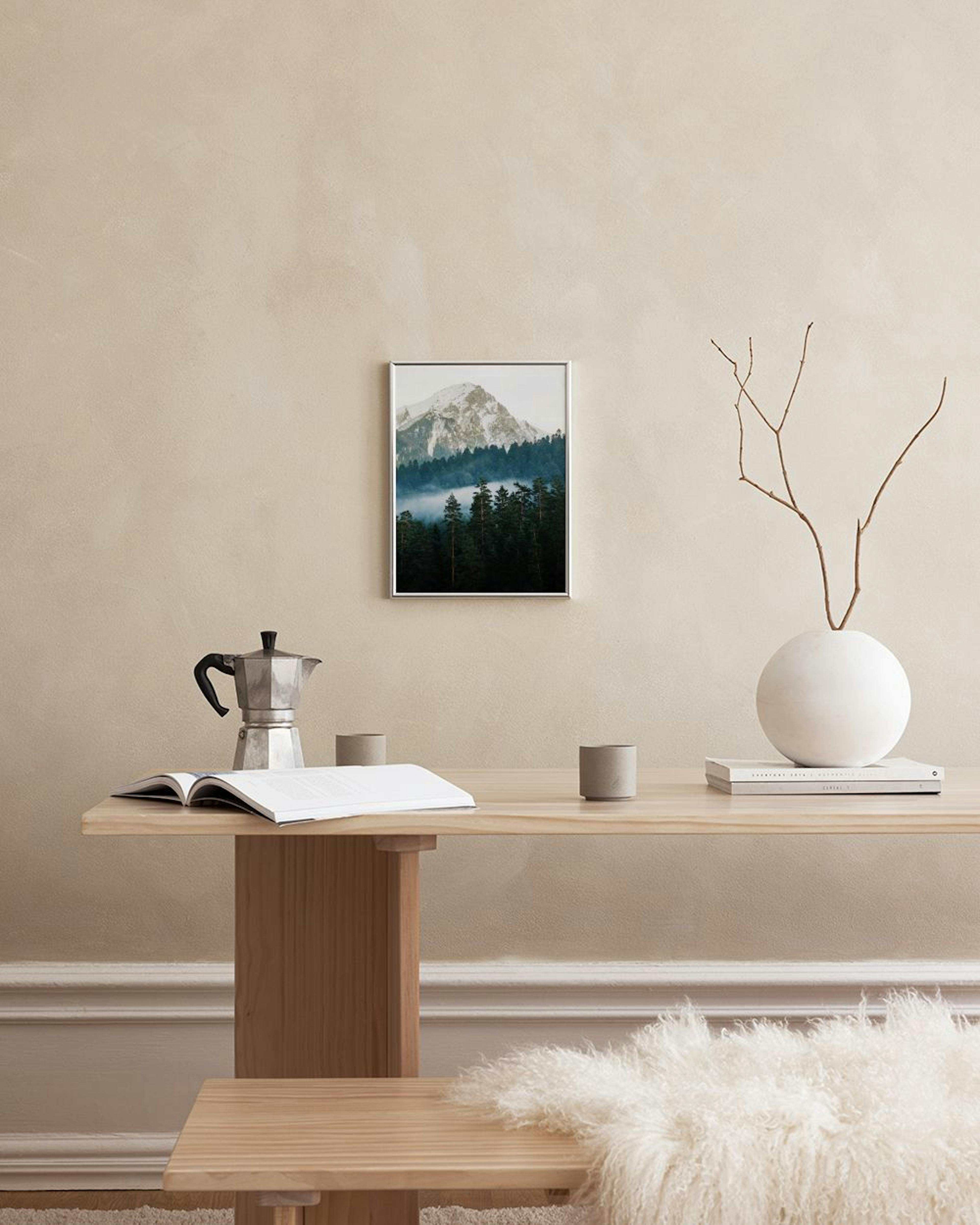 A print of a snow-capped mountain above a forest with mist, hanging above a grey cabinet with decorative vases.