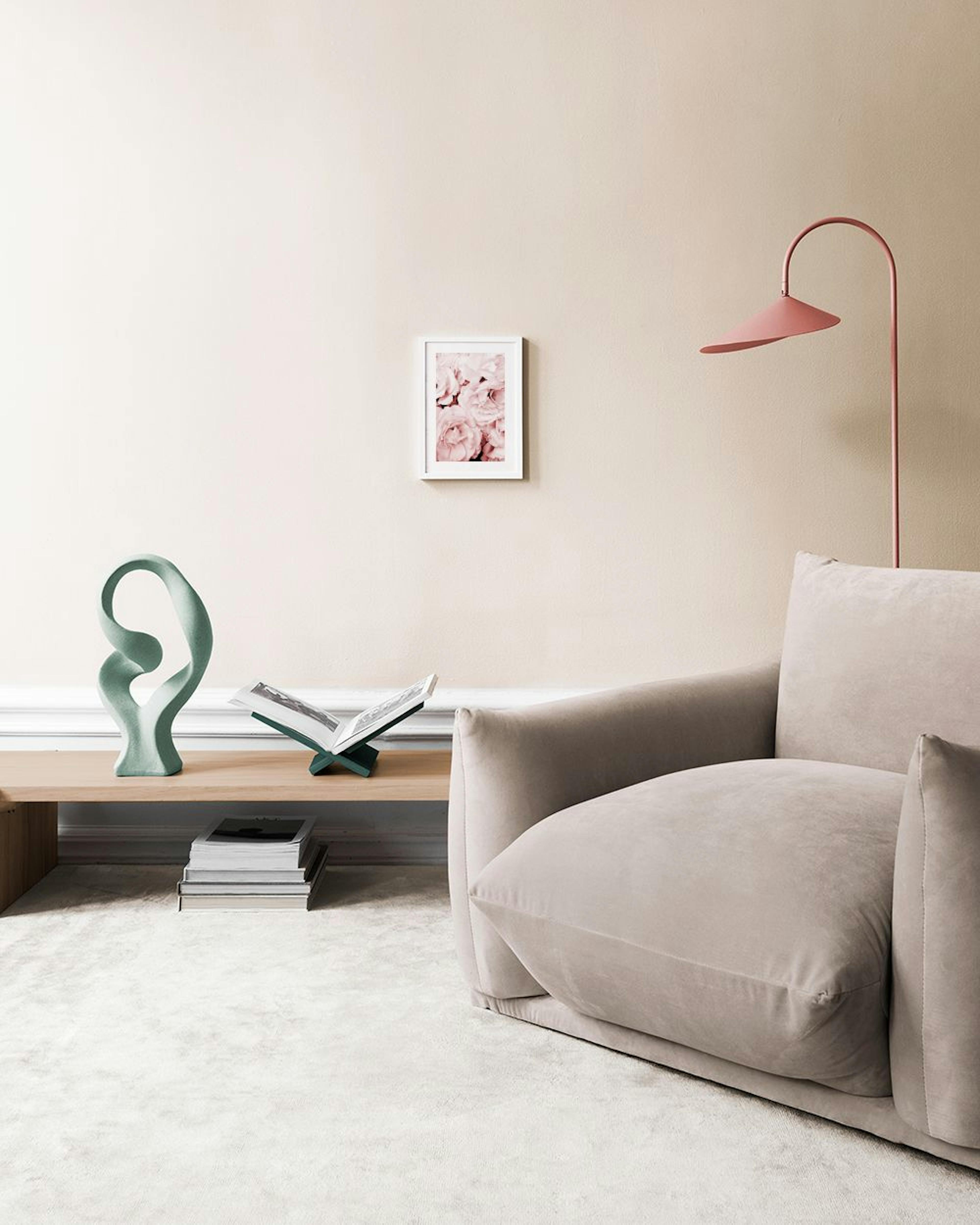 A print of soft pink roses filling the frame, displayed on a light gray wall above a pink tufted ottoman.