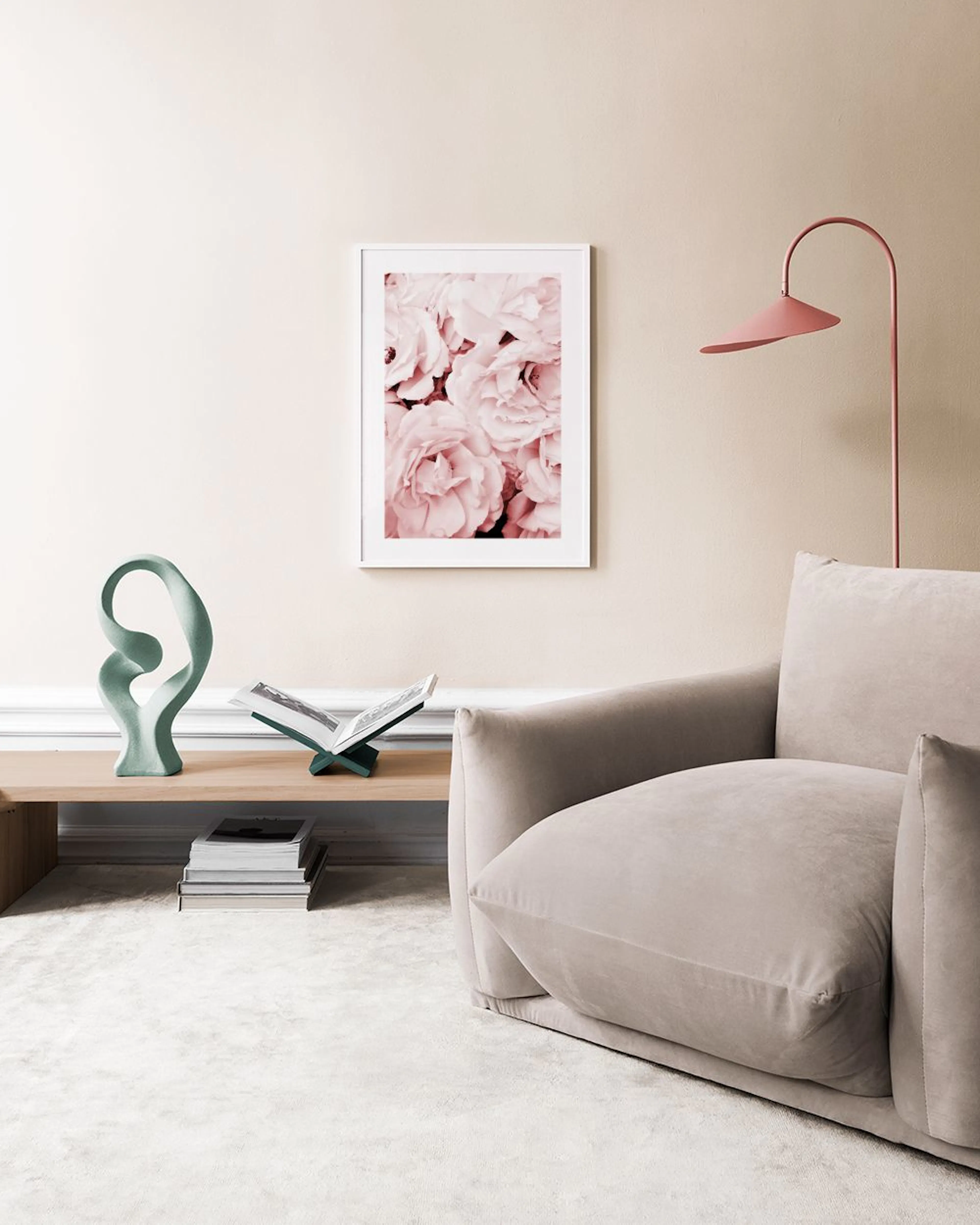 A print of light pink roses filling the frame, hanging in a room with two candle holders on grey pedestals and a pink tufted ott