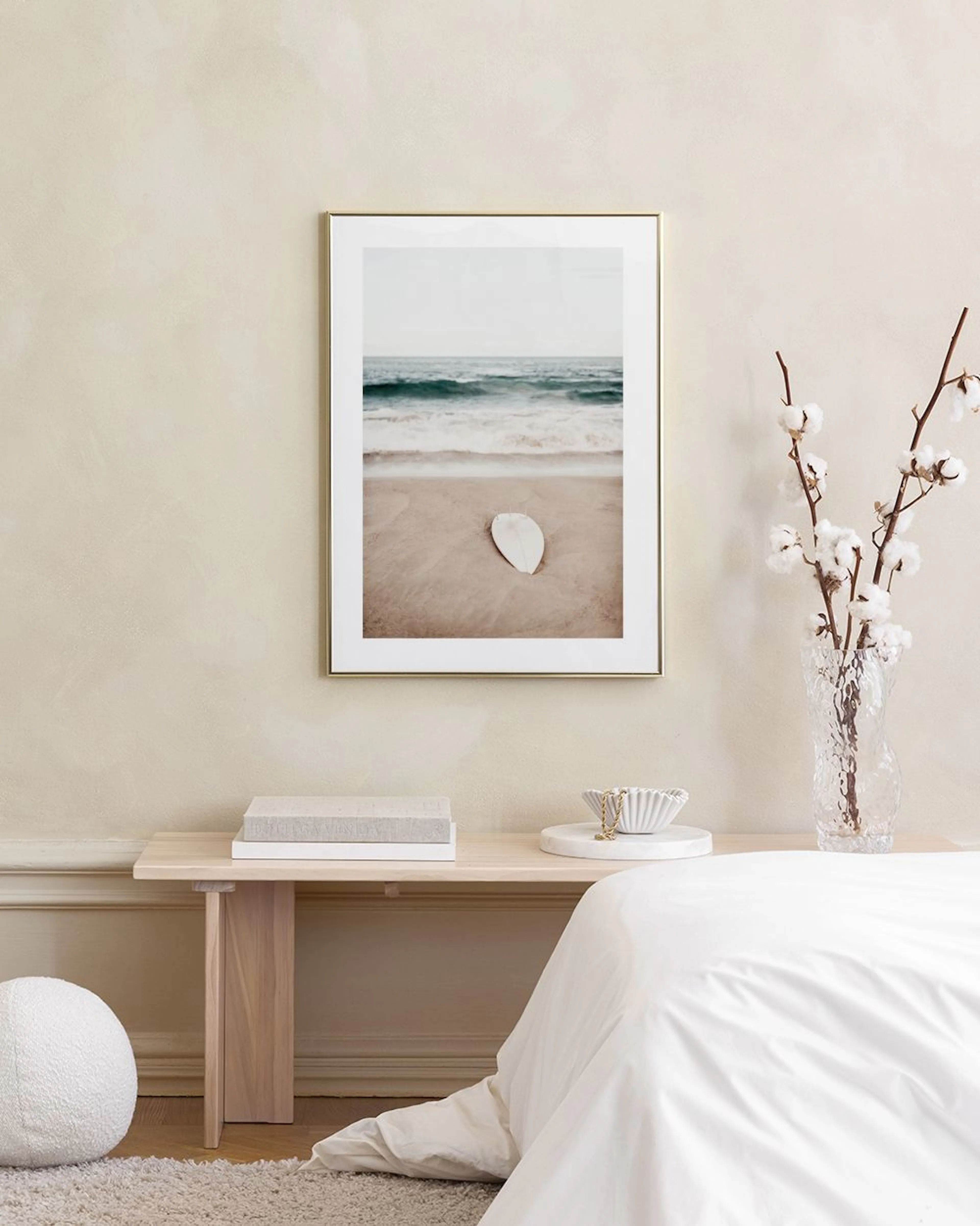 A calming beach print with a white surfboard on sand and blue waves, displayed above a teal armchair with a white pillow.