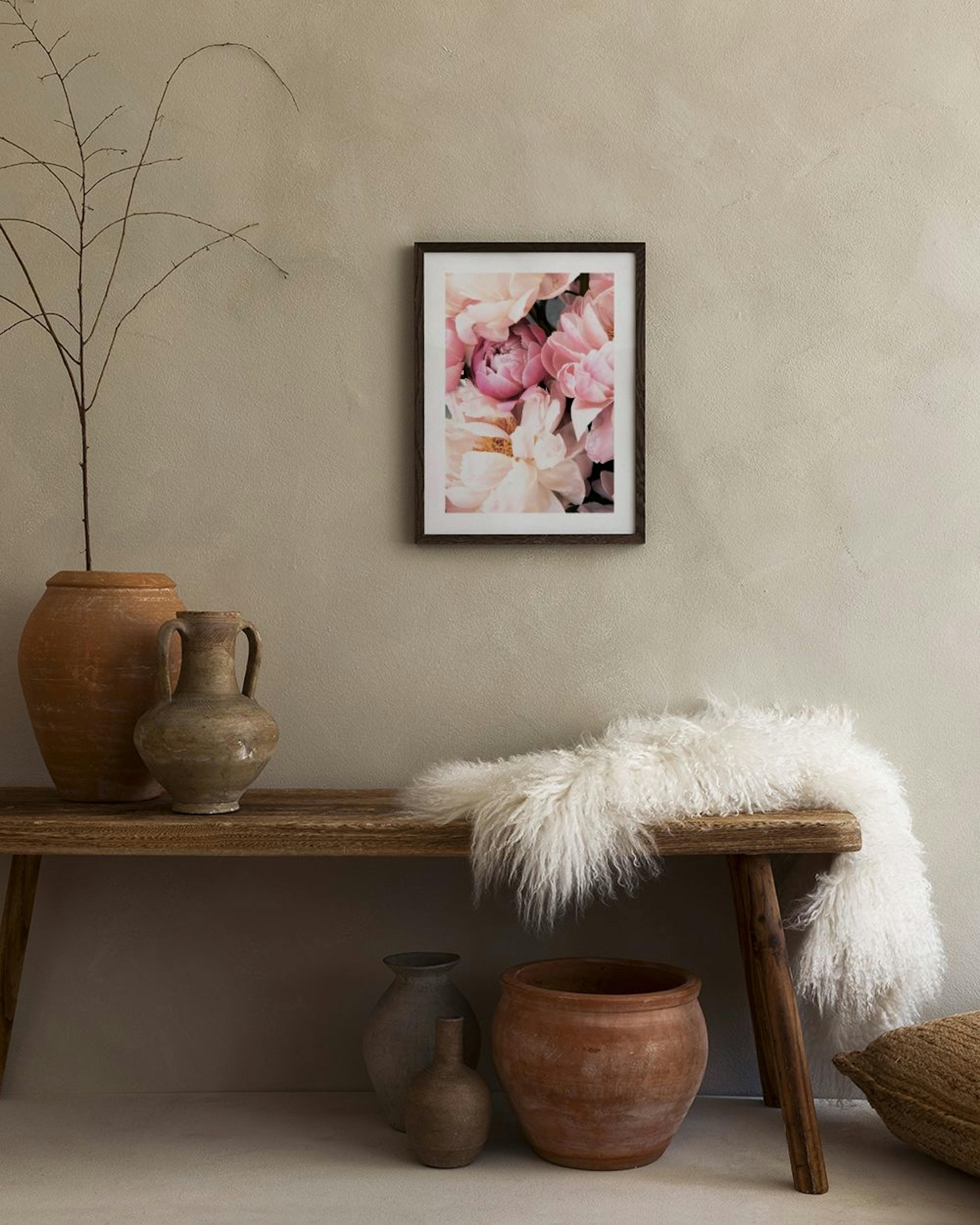 Póster de peónias cor-de-rosa e brancas, com um vaso preto, bola de betão e livro aberto numa mesa, ao lado de uma cadeira de ve