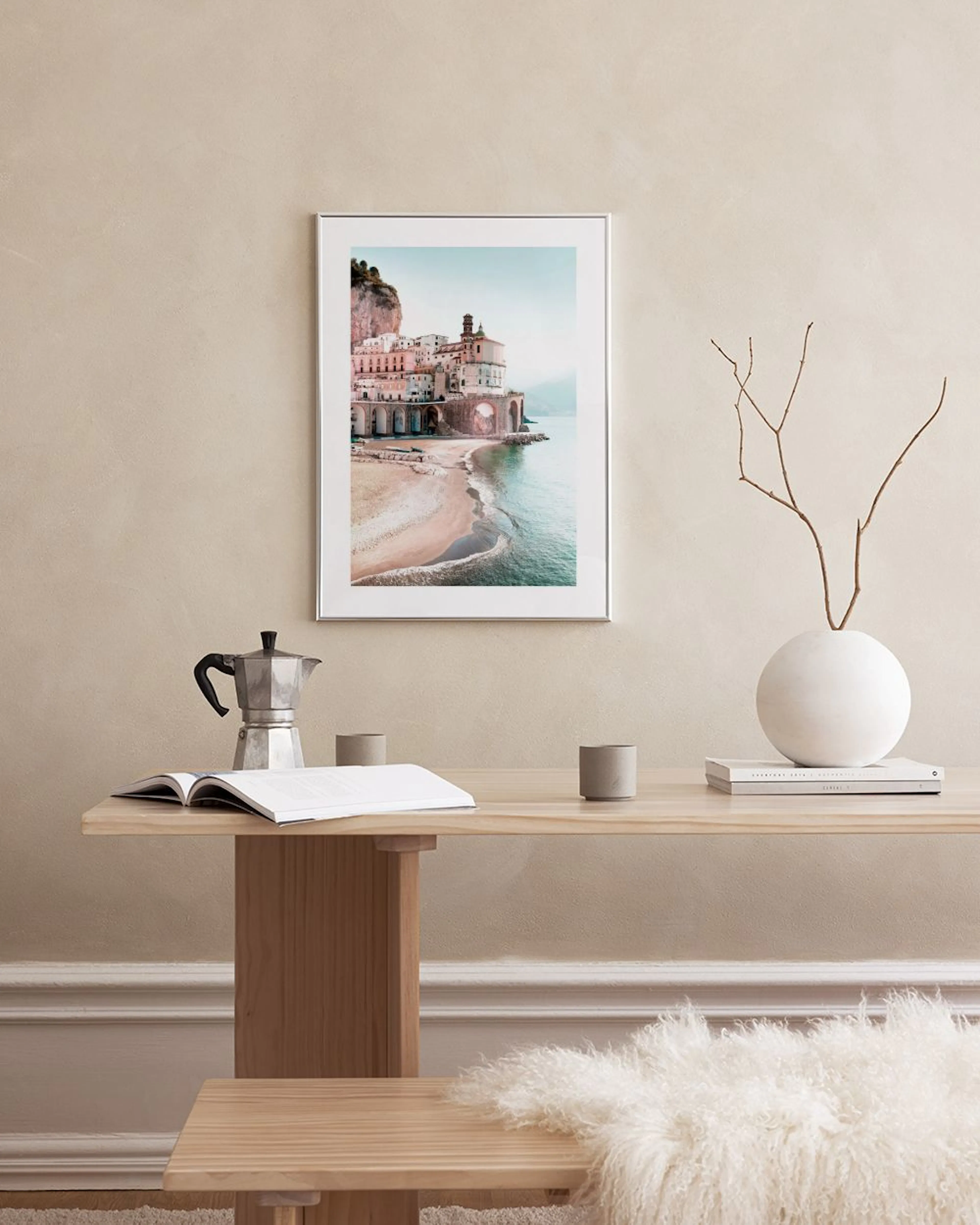 Póster de un pueblo costero con edificios históricos rosados, una playa de arena y el mar, colgado sobre un escritorio de madera