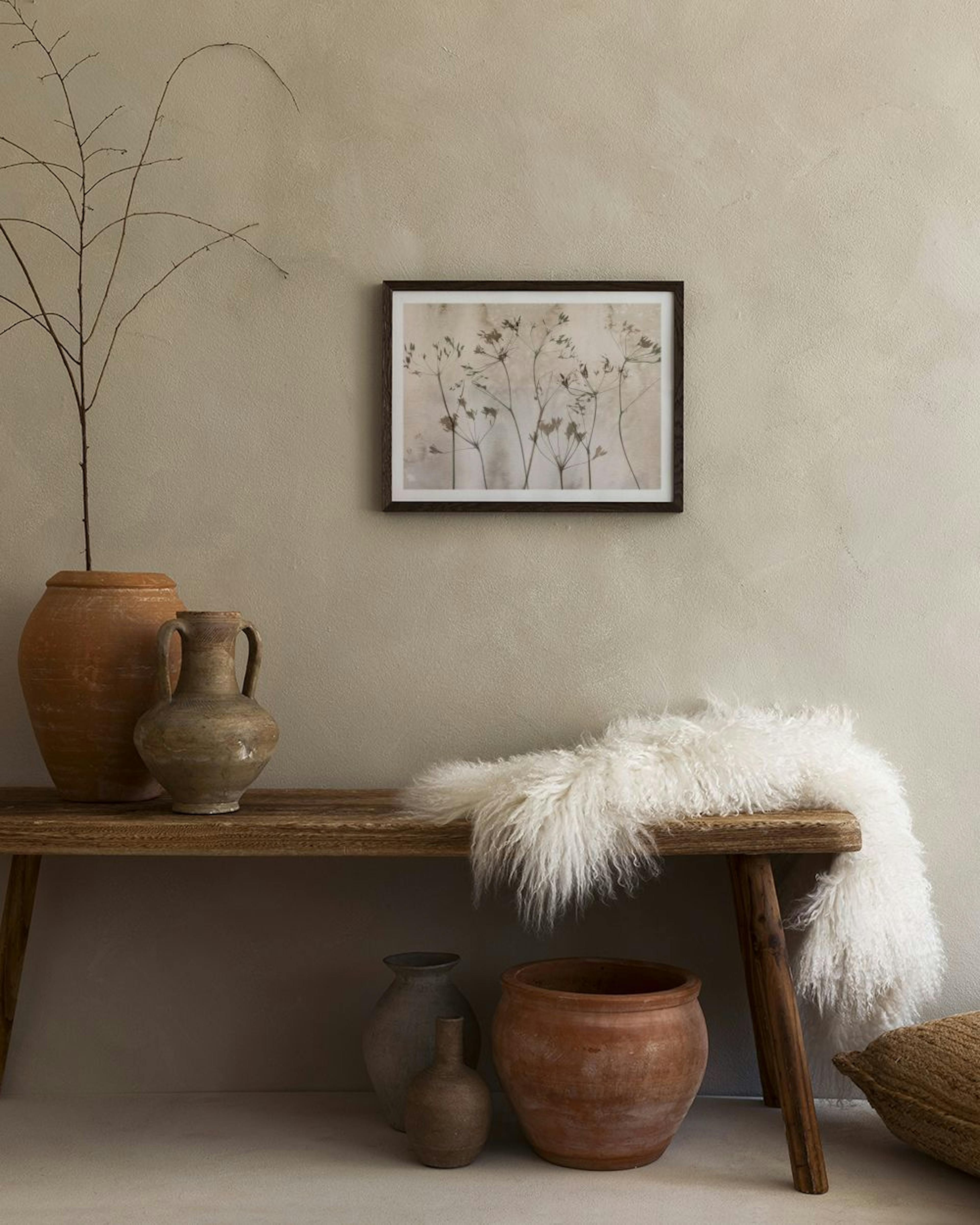 Botanical print with dark silhouettes of wild plants on a beige textured background, hanging above a light beige sofa.