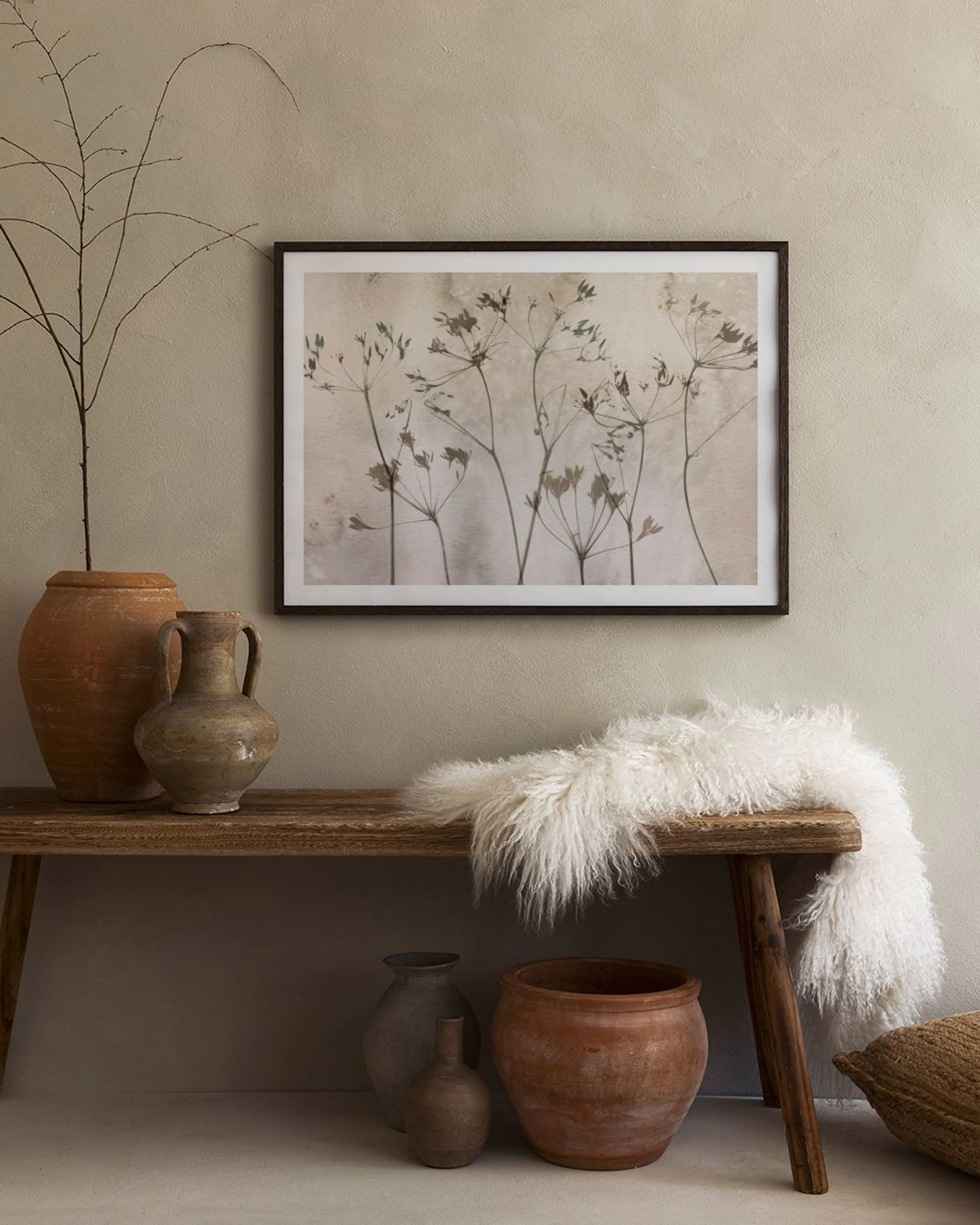 Poster med silhuetter av torkade växter i neutrala toner, hängandes ovanför en beige soffa i ett vardagsrum.