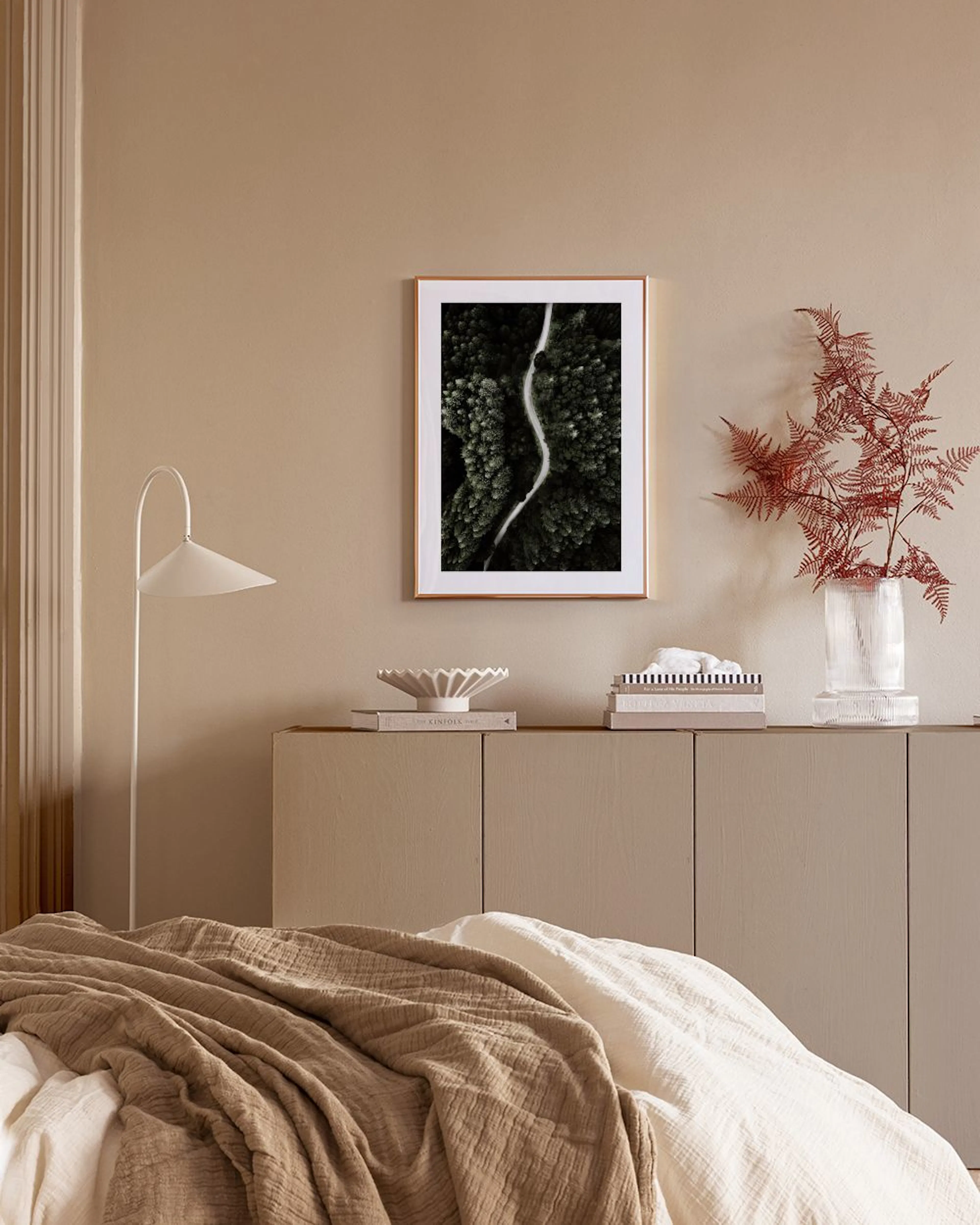 An aerial print of a winding road through a dark green forest, hanging above a white console table in a modern living room.