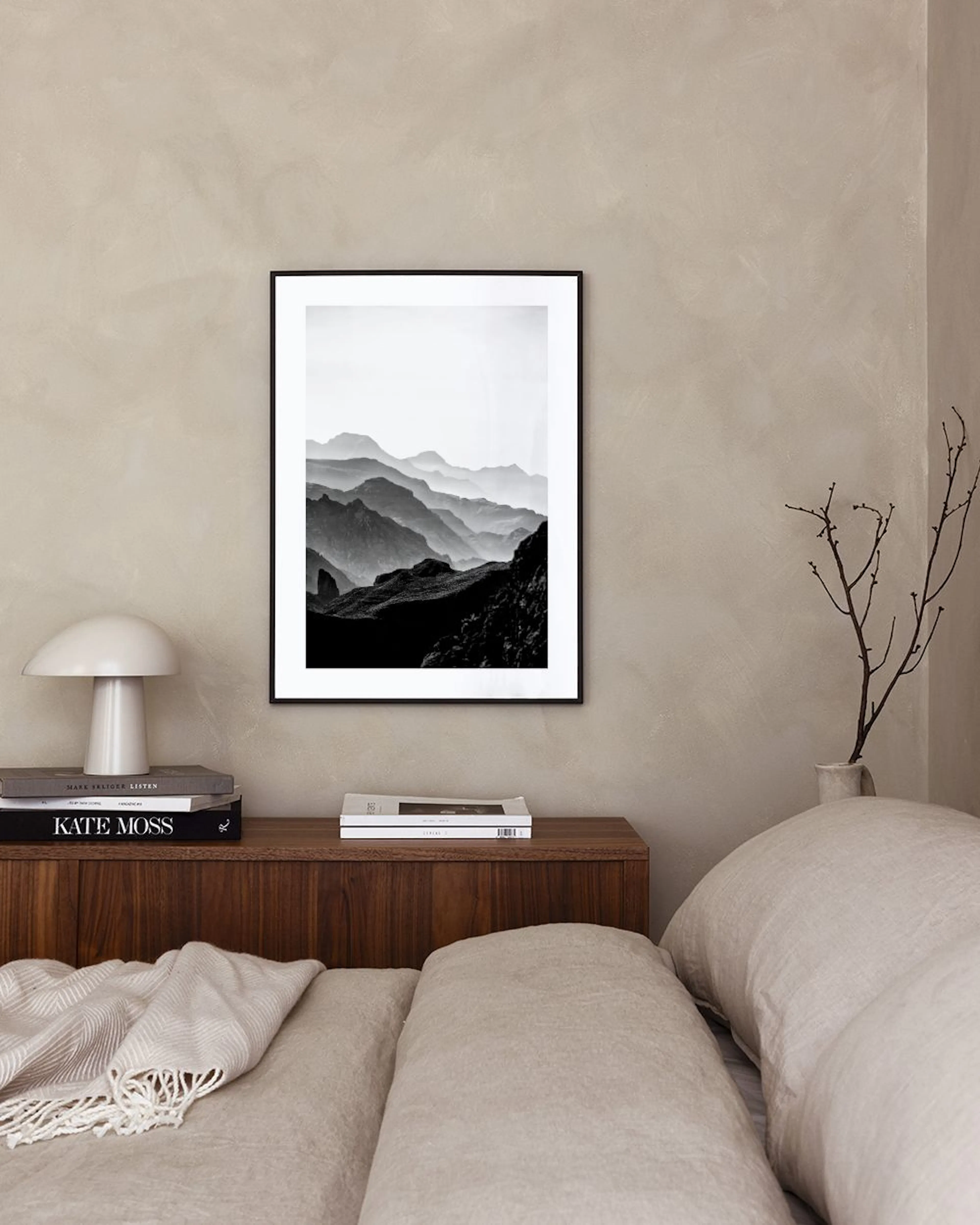 Zwart-wit poster van berglandschap met mistige toppen, hangend boven een wit dressoir met vaas en naast een blauwe stoel.