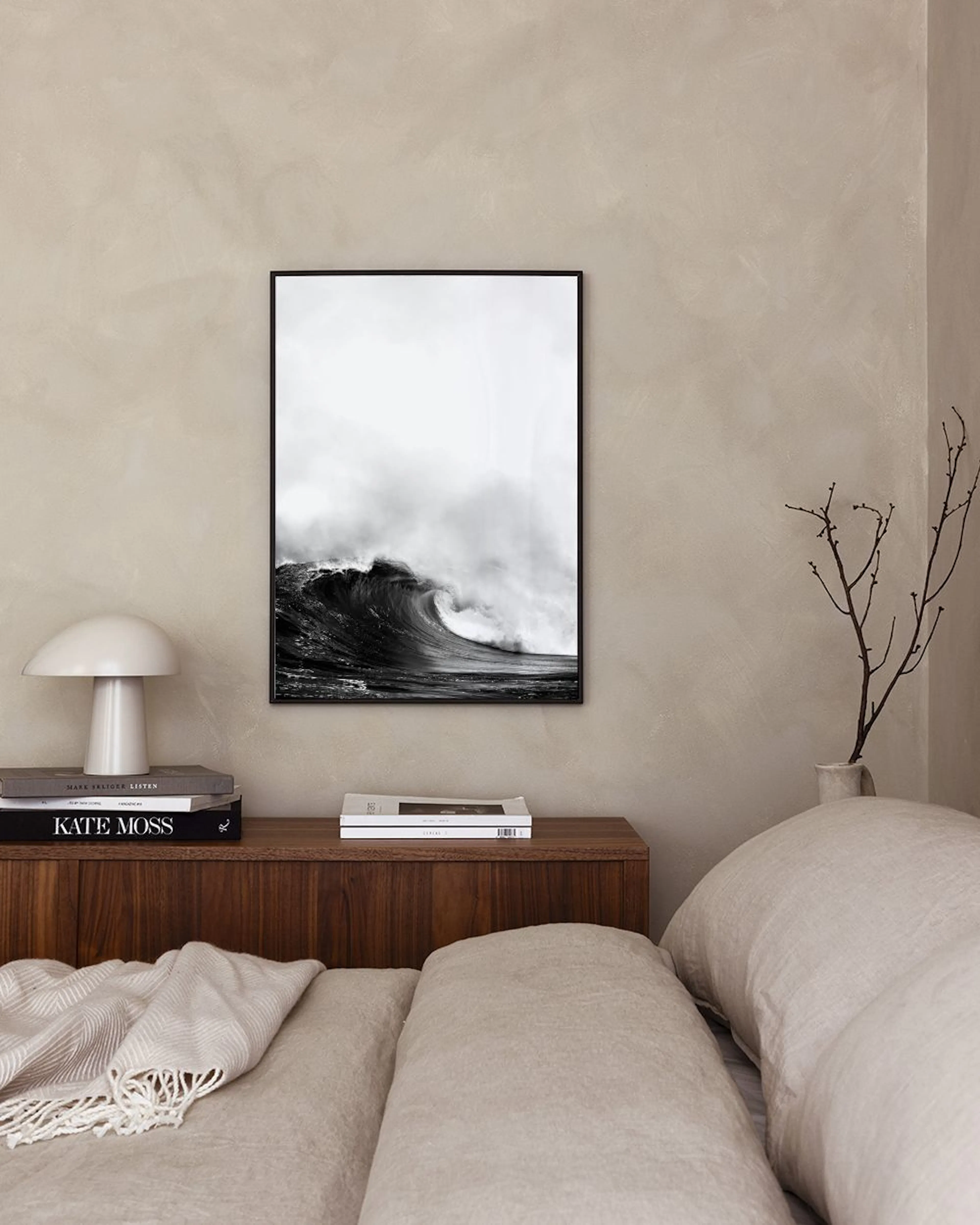 A stunning monochrome print of a powerful ocean wave, displayed on a dark blue wall with two decorative glass bottles and a thro