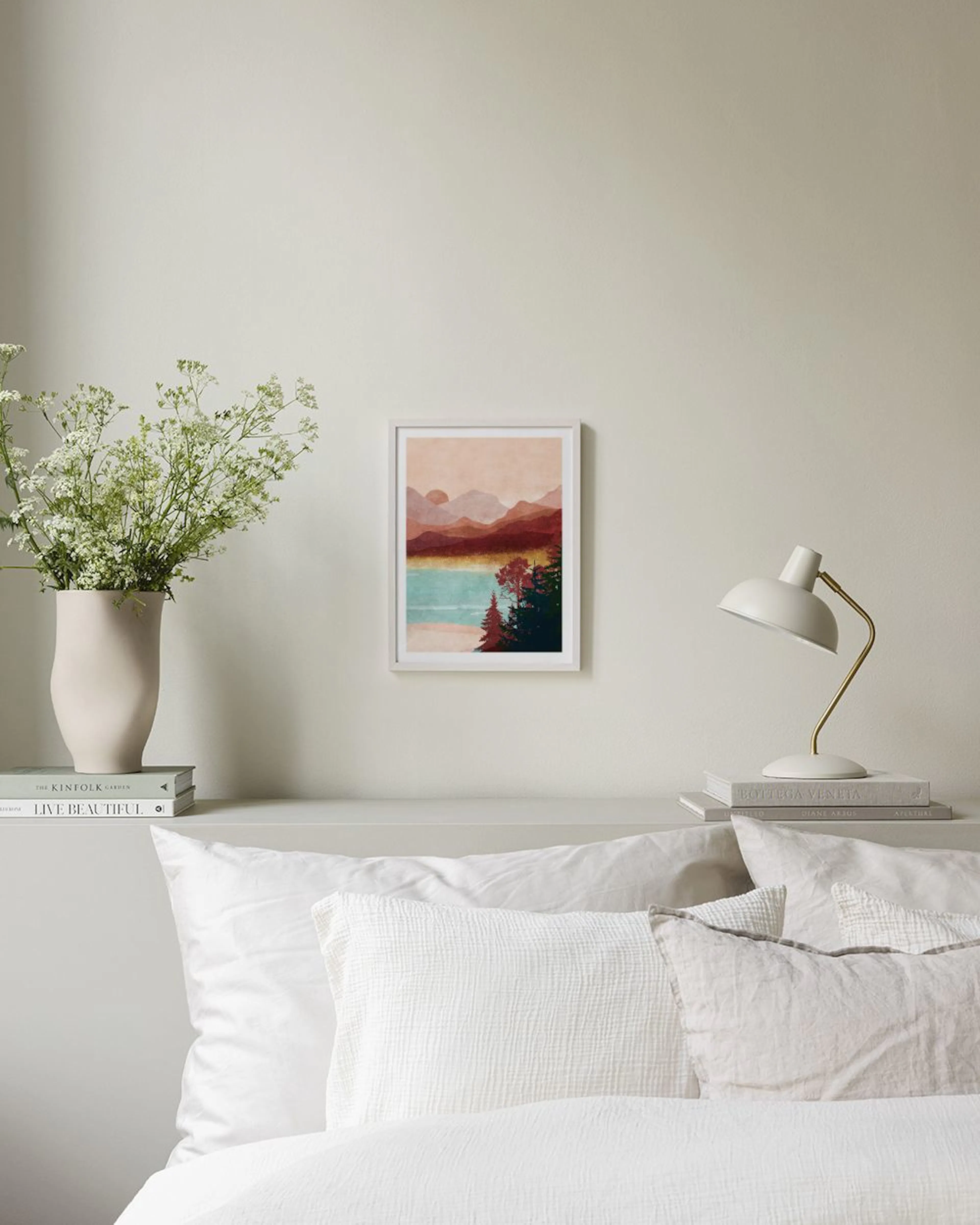 Poster mit Berglandschaft, See und Wald in warmen Erdtönen und Türkis, hängend über einem weißen Sideboard mit Vase und Büchern.