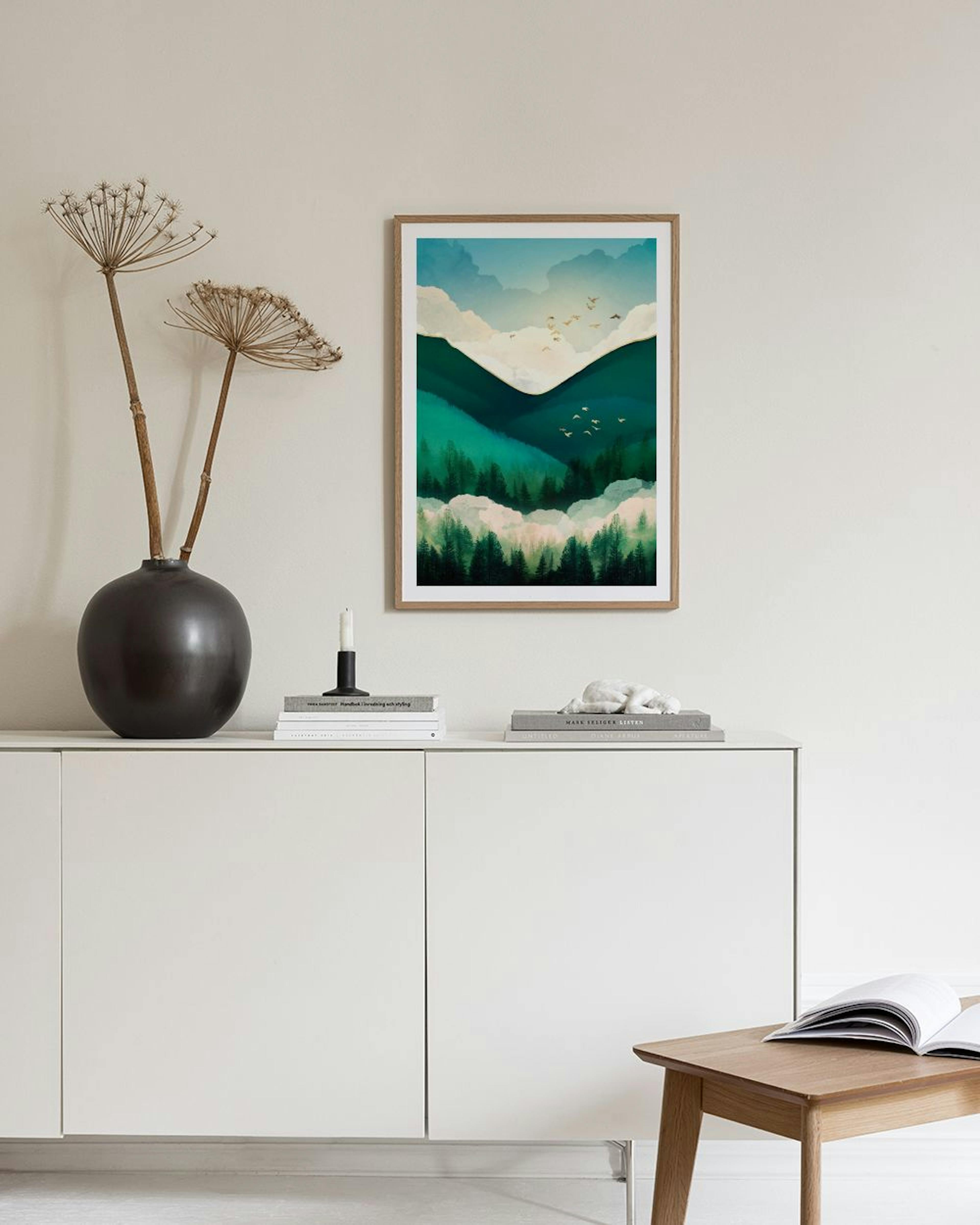 A nature print of green mountains and forests with birds flying in a cloudy sky, hanging above a white console table with a vase