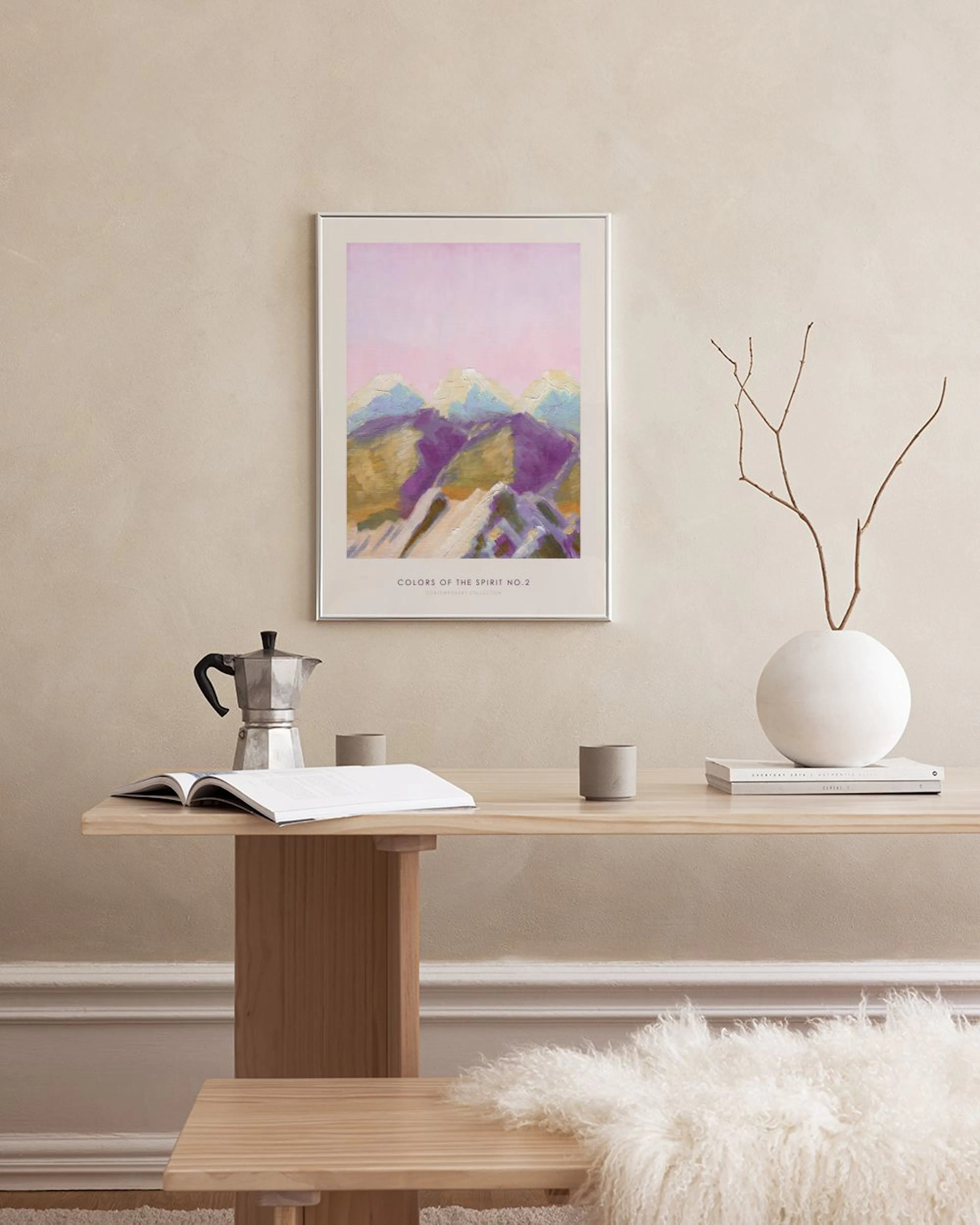 A poster of impressionistic mountains with purple and gold hues under a pink sky, hanging above a white marble table with vases 