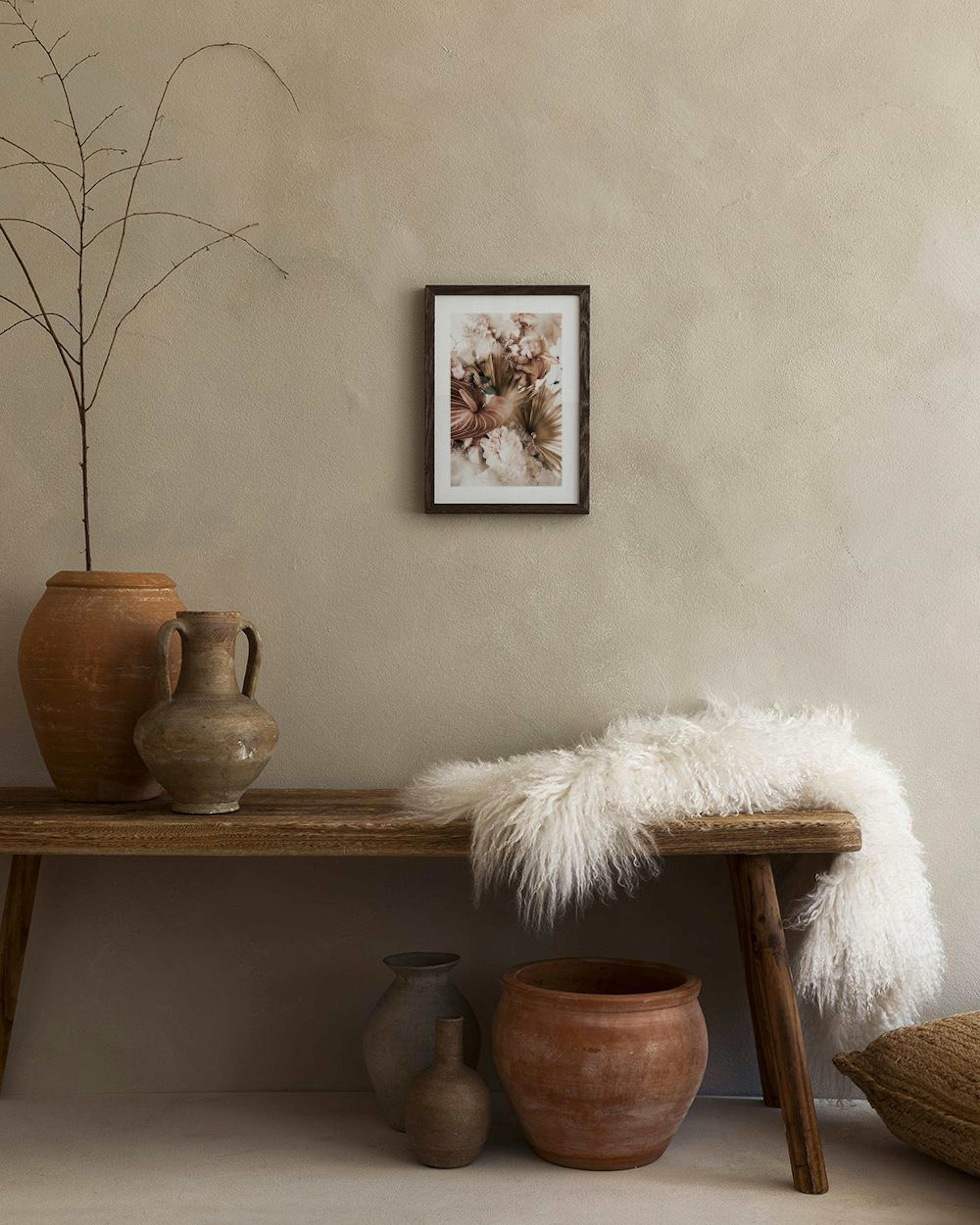 A floral print with pink and brown flowers and leaves, hanging in a bedroom above a bed and black nightstand.