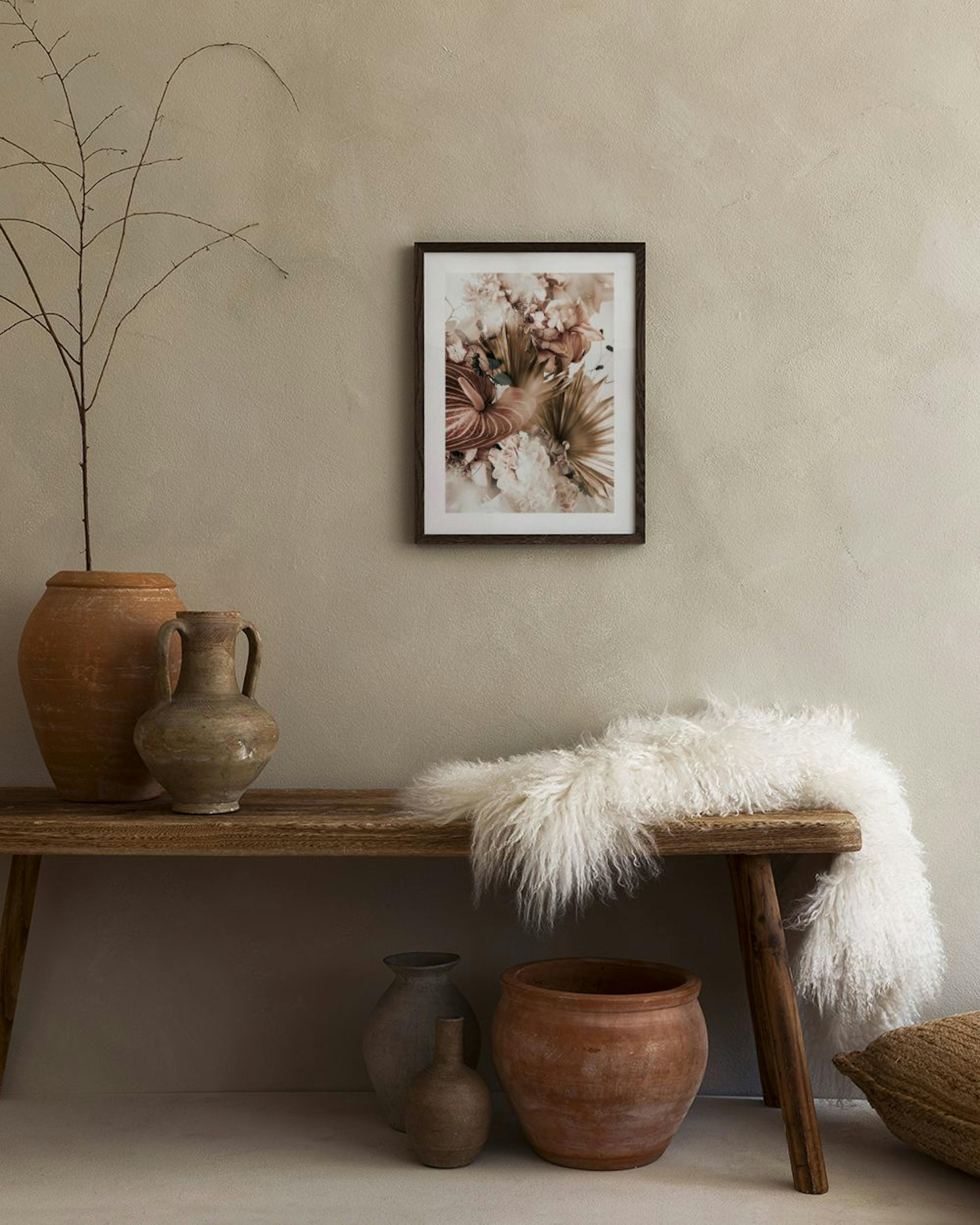 Floral print with anthurium, palm leaves, and peonies in warm nude tones, hanging above a bedside table in a bedroom.