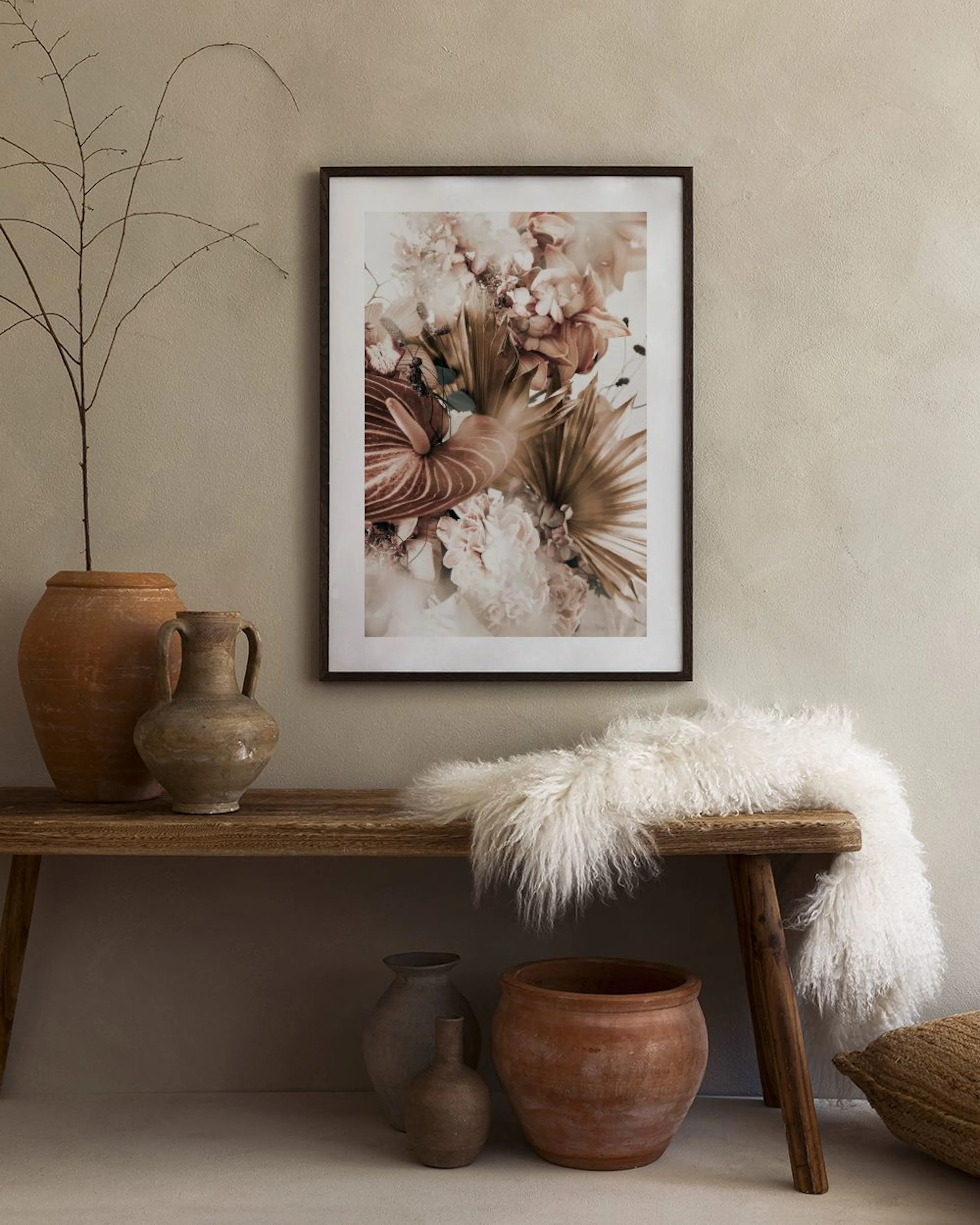 A floral print with pink and brown flowers and leaves, hanging in a bedroom above a bed and black nightstand.