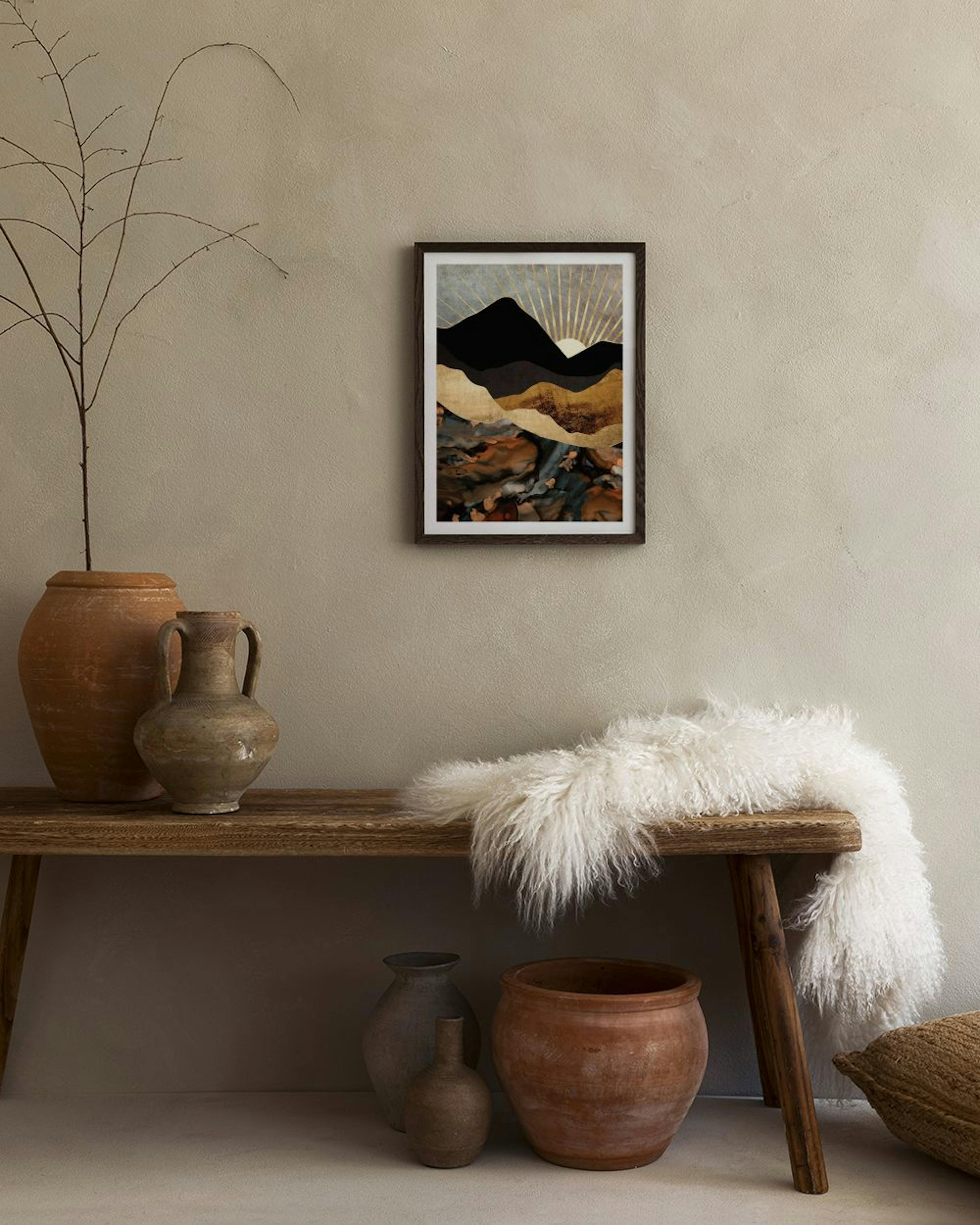 Póster de paisaje con montañas negras y doradas, y un sol naciente con rayos dorados, colgado sobre un mueble oscuro con libros 