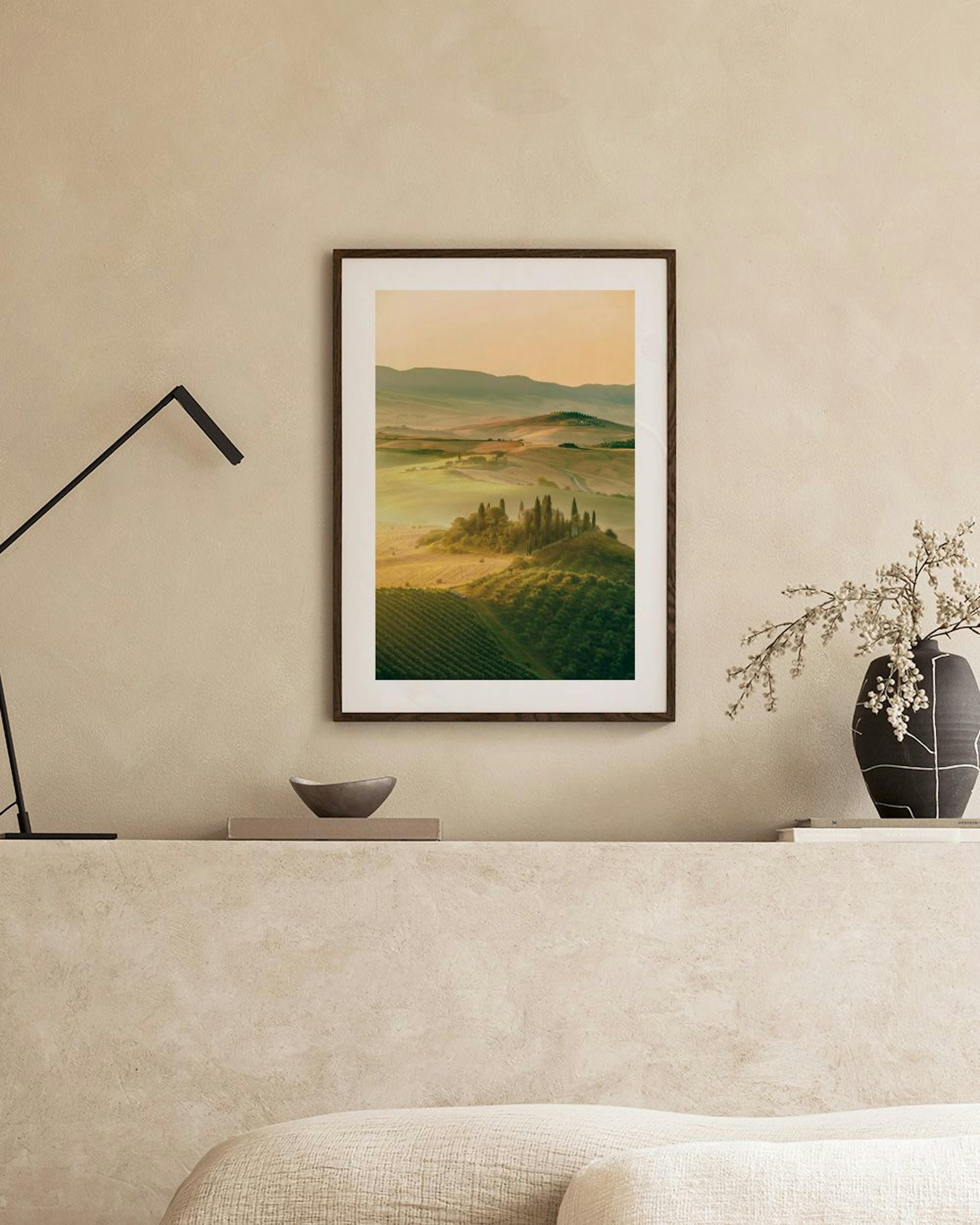 Póster de paisagem rural toscana com colinas verdejantes e ciprestes, pendurado acima de um móvel de vime.