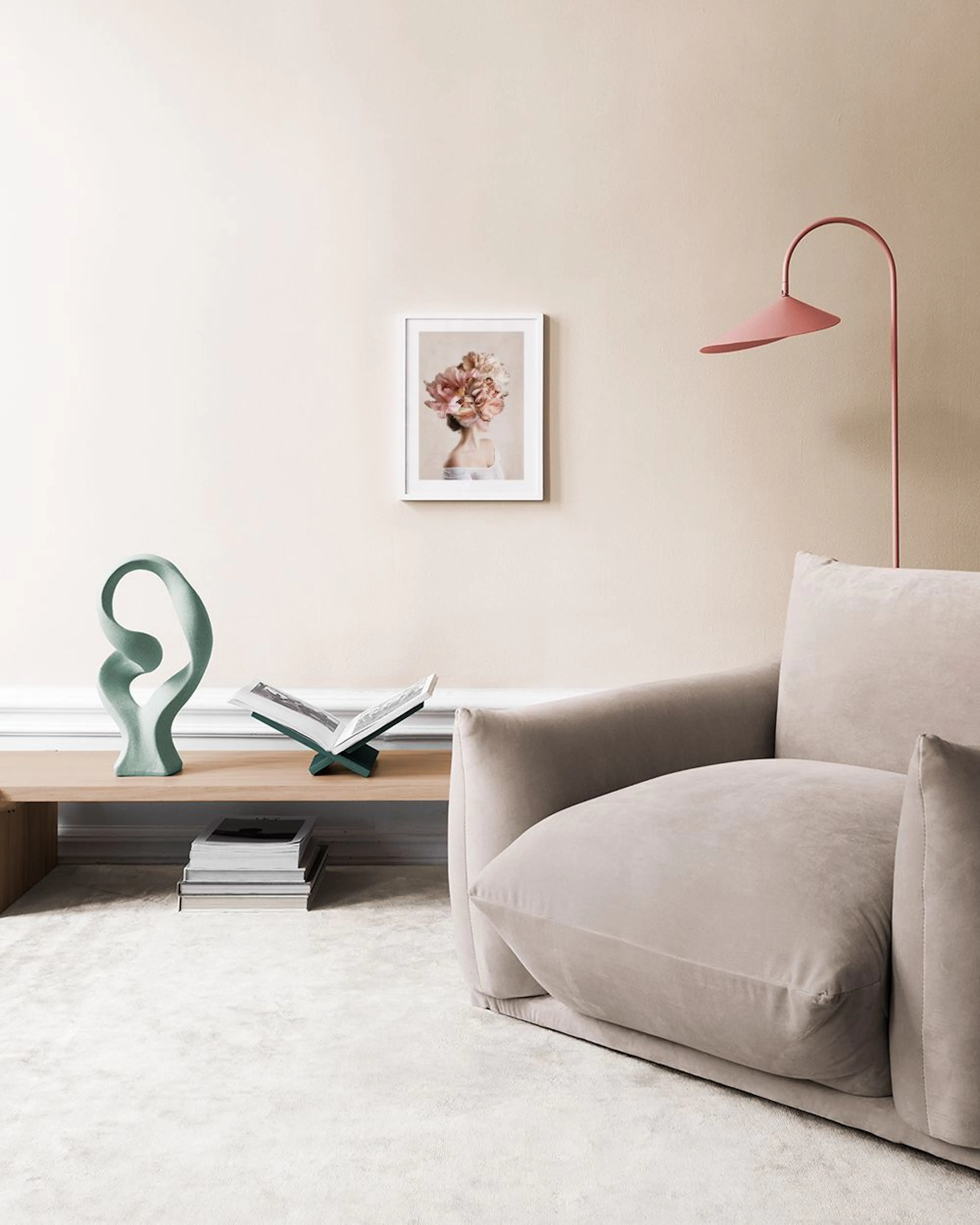 A print of a woman with large, soft pink and beige flowers covering her head, hanging above a white side table with two vases an