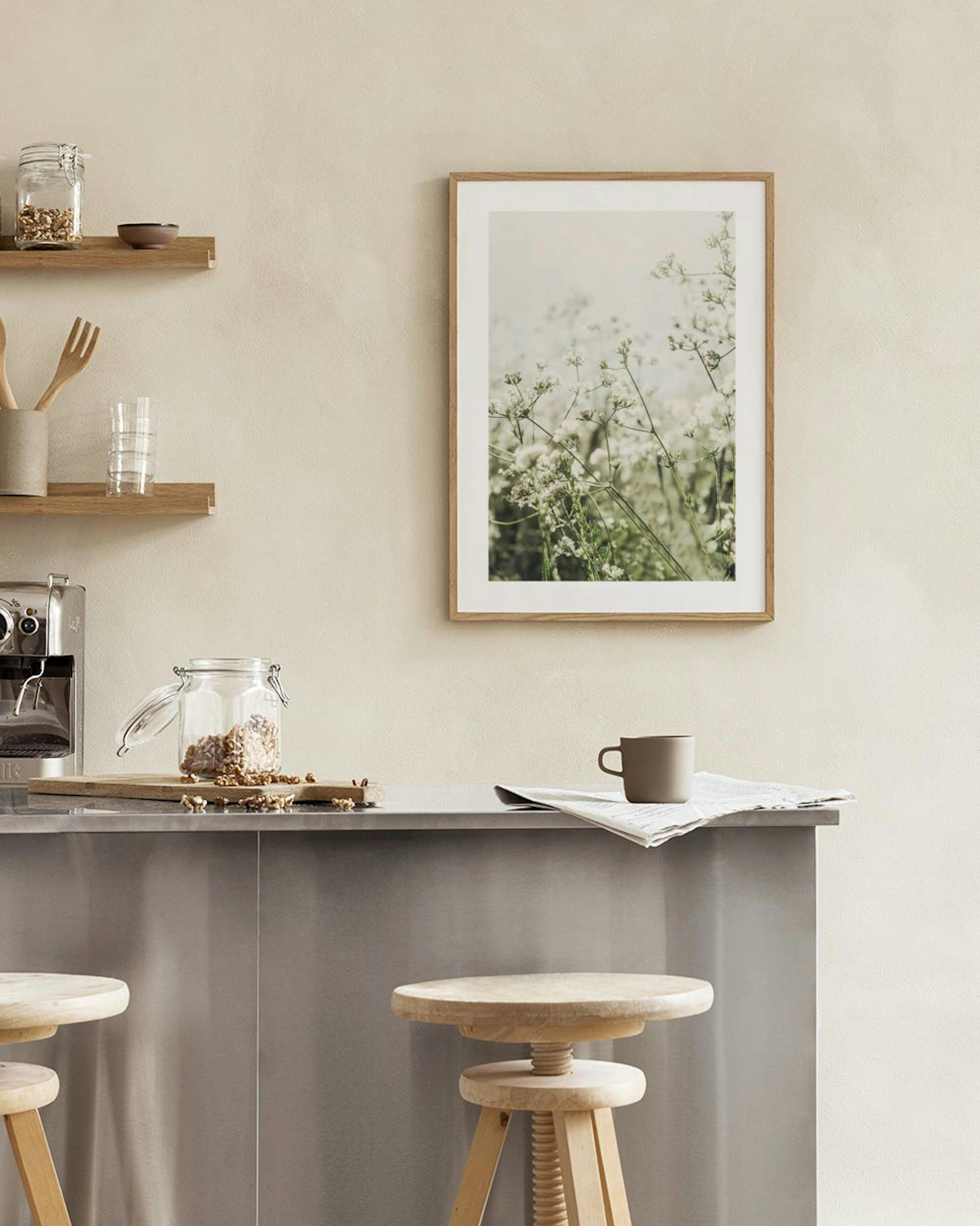 Poster van witte weidebloemen op een lichte achtergrond, hangend boven een wit dressoir met een glazen vaas en een open boek.