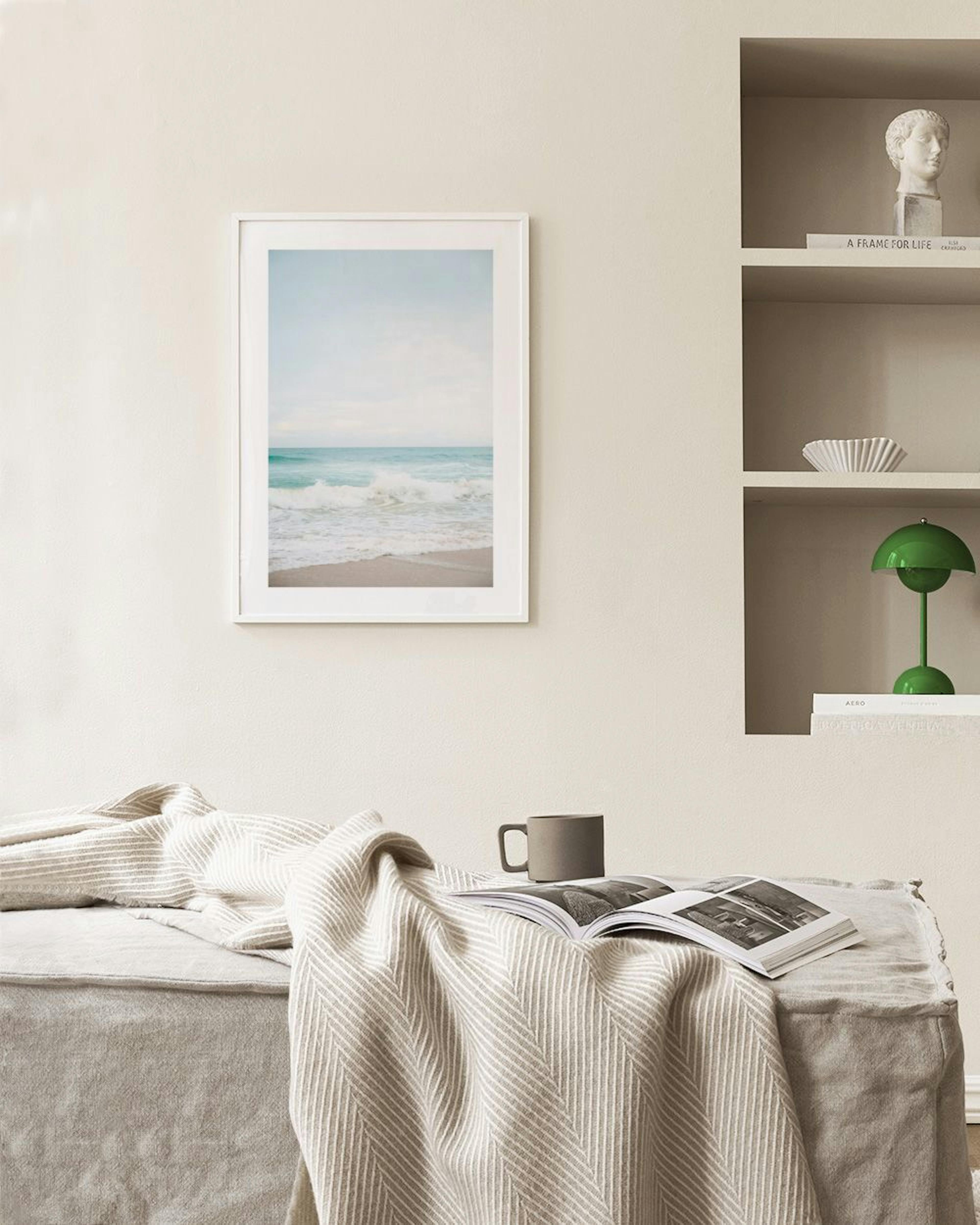 Poster van een kalme oceaan met golven op het strand, hangend boven een blauwgrijze fluwelen stoel.