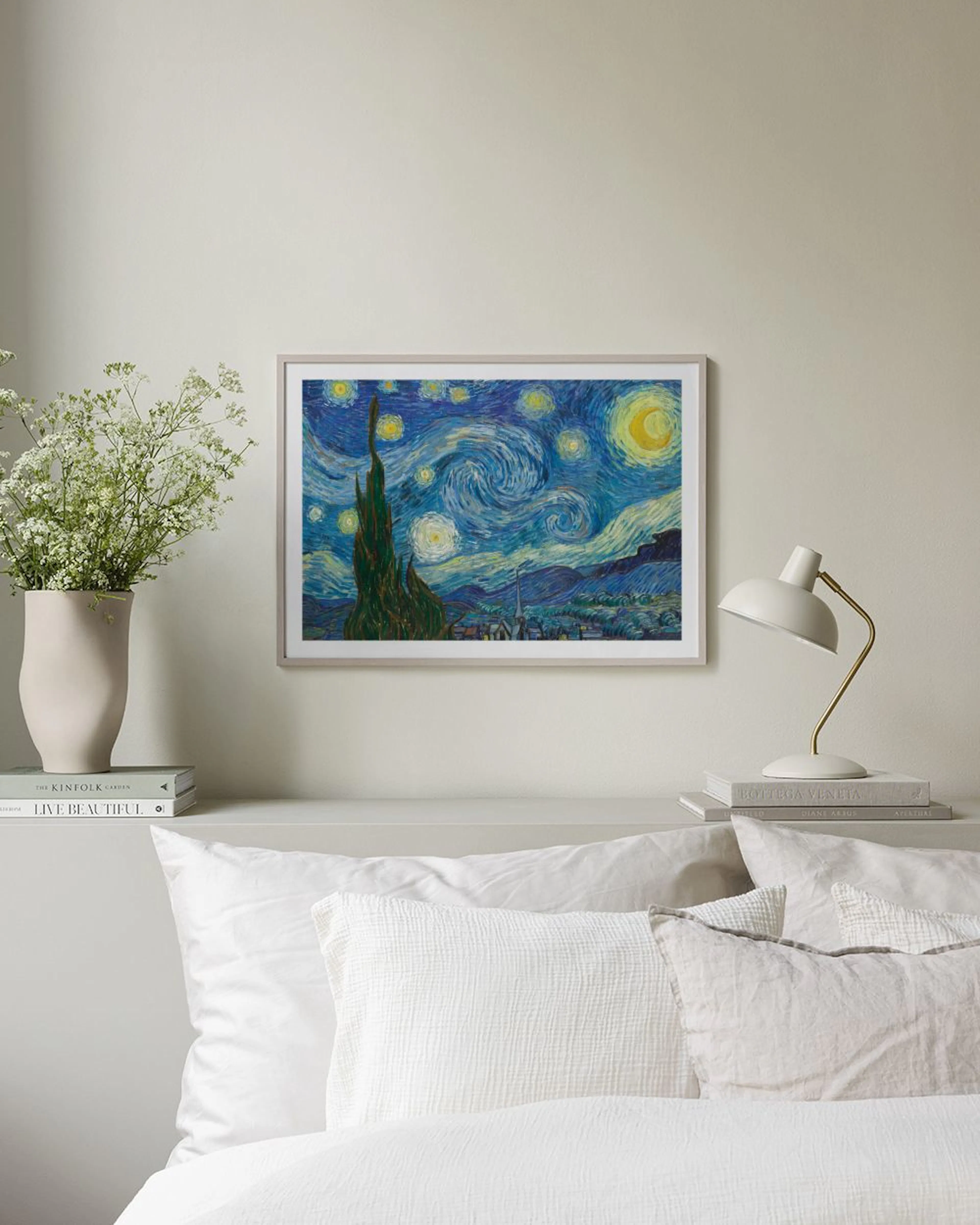 A print of Van Goghs Starry Night with a swirling blue sky, dark cypress tree, and yellow moon, hanging in a modern living room.