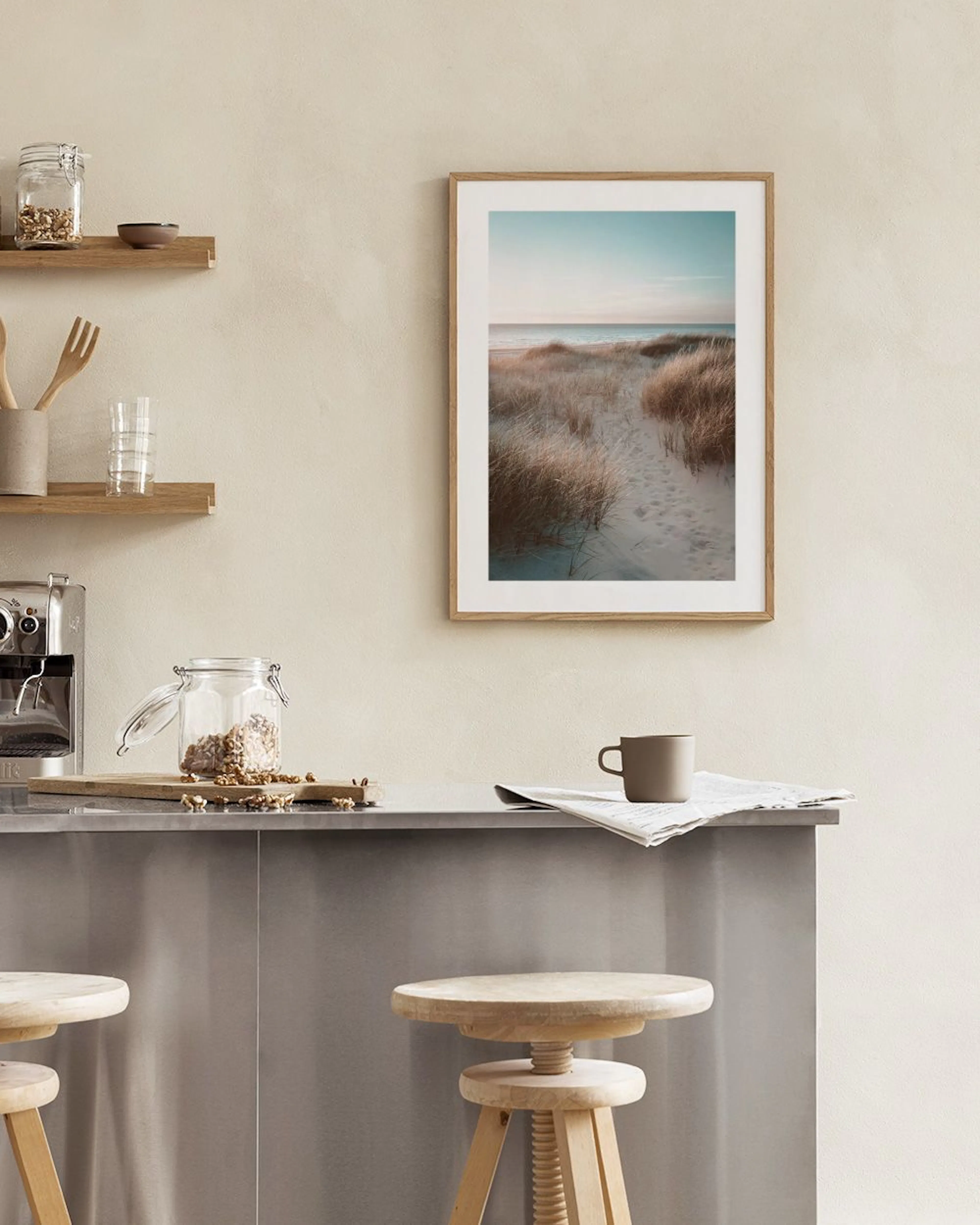 Póster de dunas de arena con hierba seca y un sendero hacia el mar, exhibido en una sala de estar minimalista.