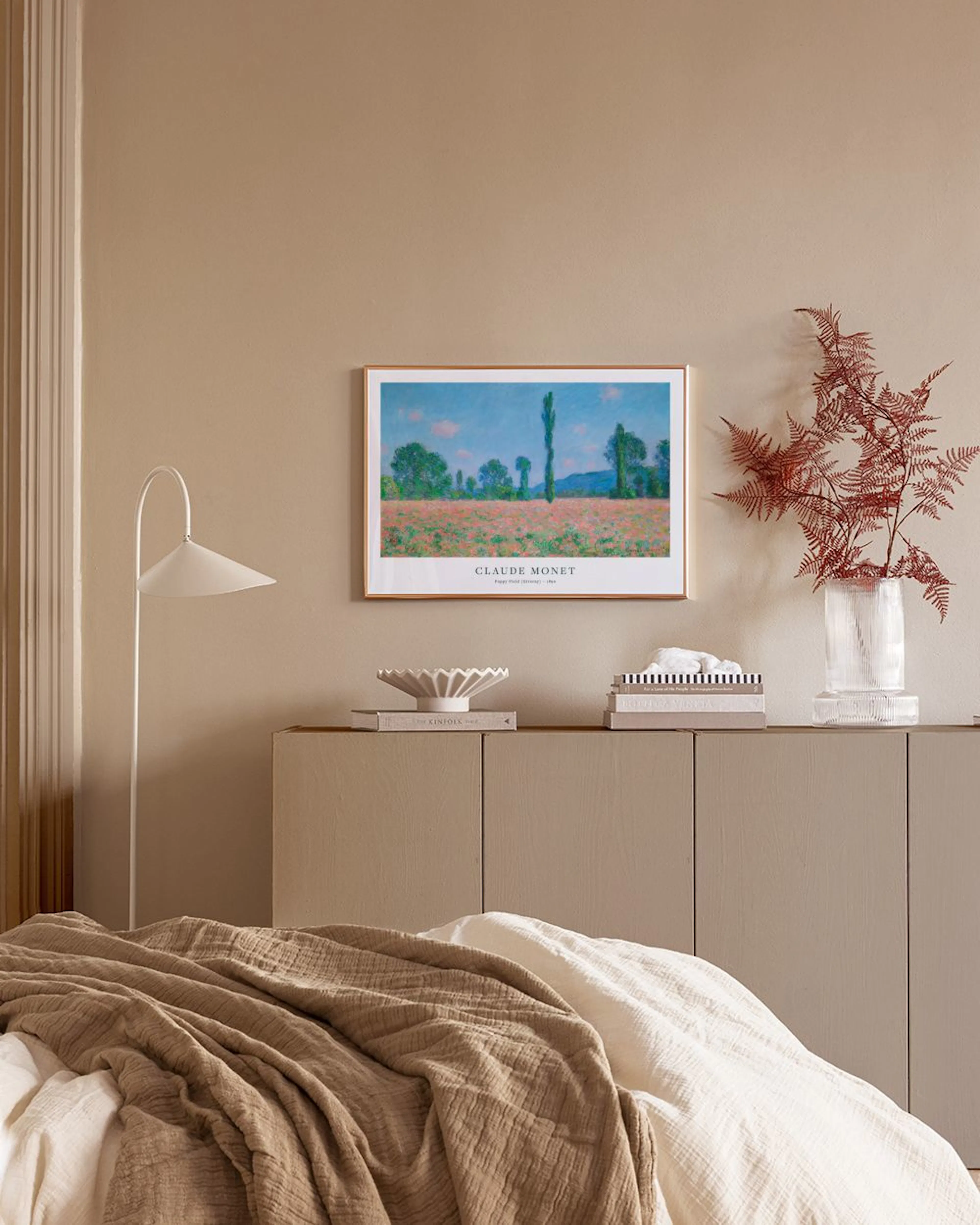Affiche Champ de coquelicots de Monet sur mur blanc, au-dessus dun meuble avec vase et livres.