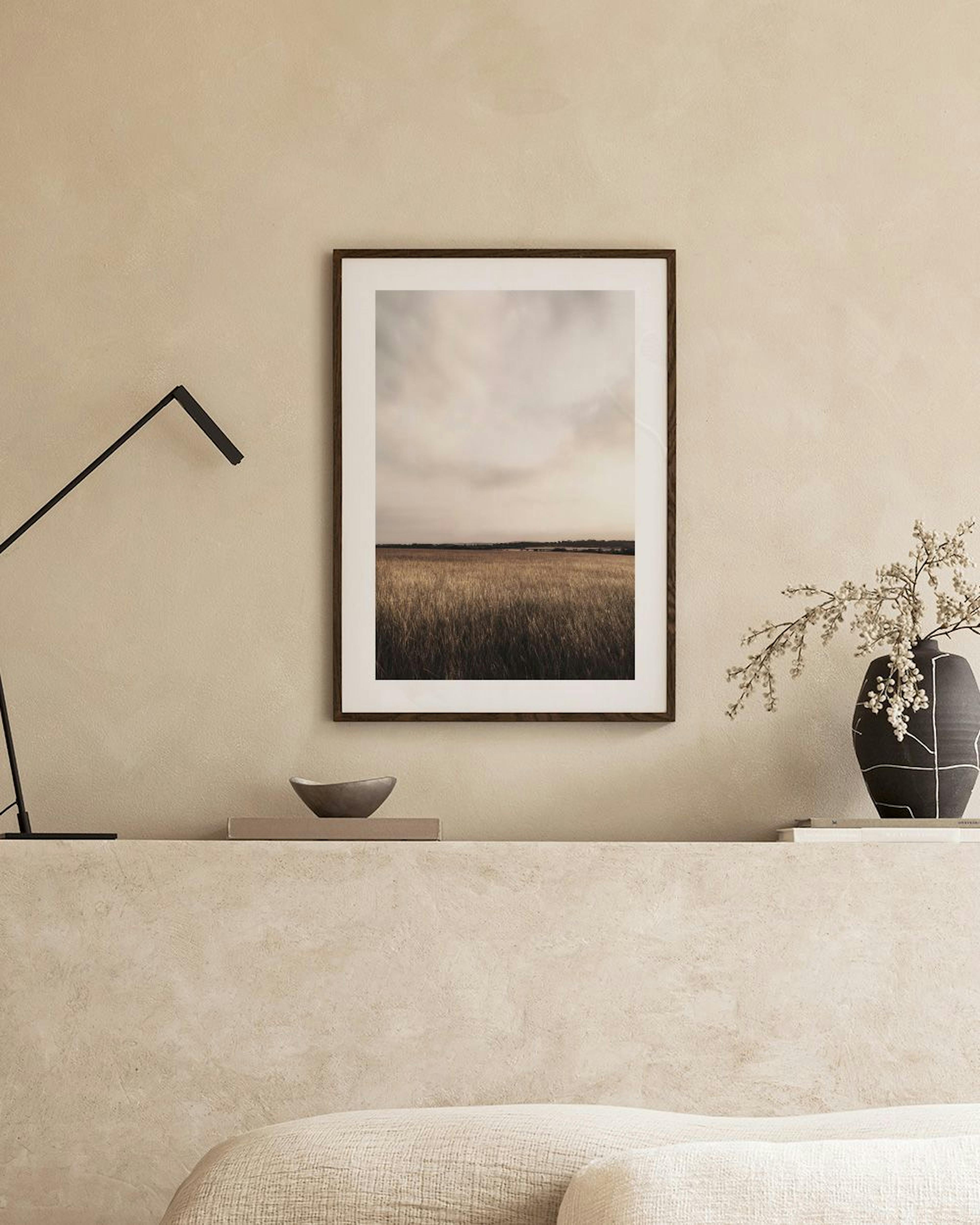 Poster con paesaggio di campo di erba alta sotto un cielo nuvoloso, appeso su una parete beige in un ambiente moderno.
