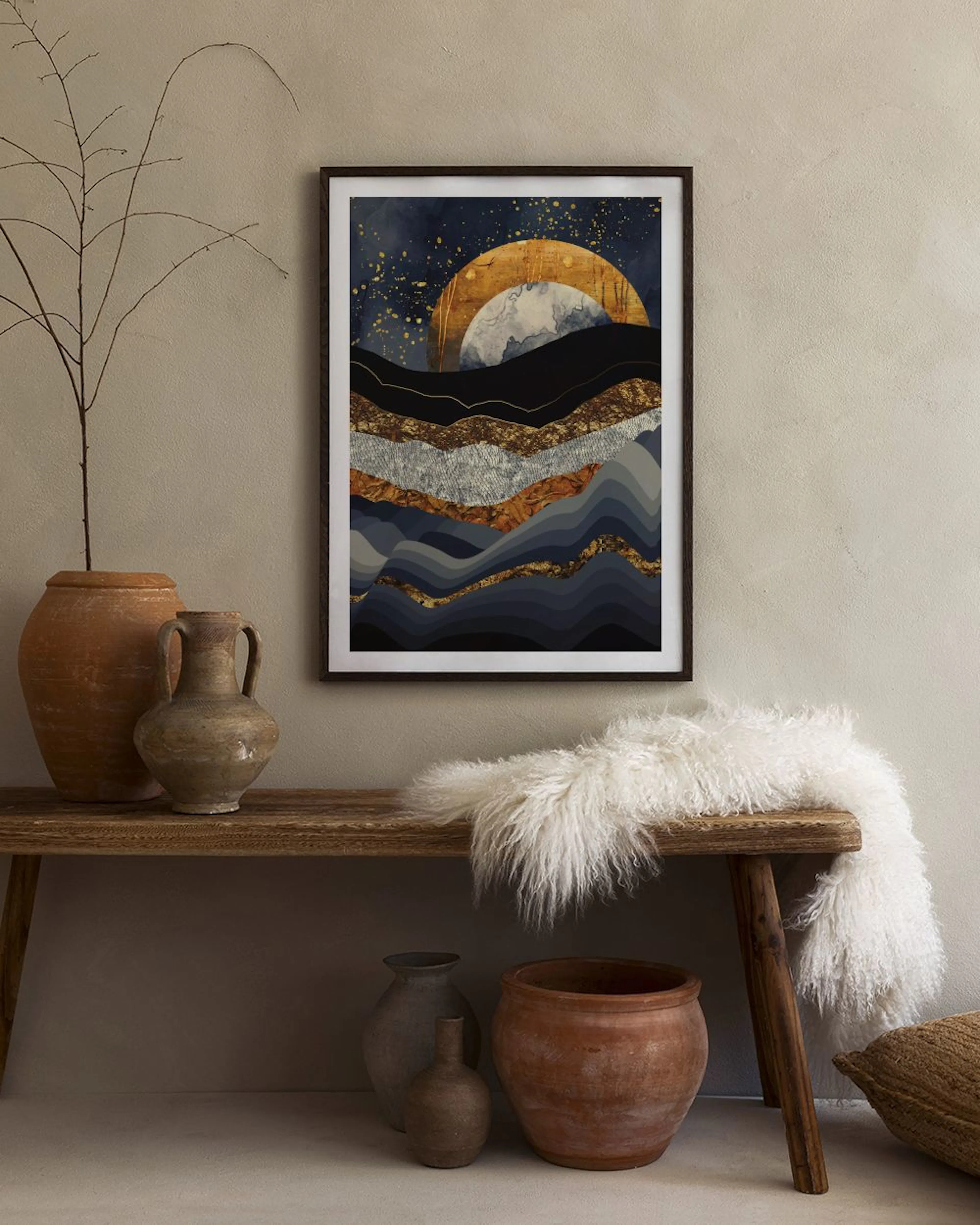 Póster de paisaje abstracto con montañas de tonos azules, grises y dorados, y un sol brillante, colgado sobre una mesa negra con