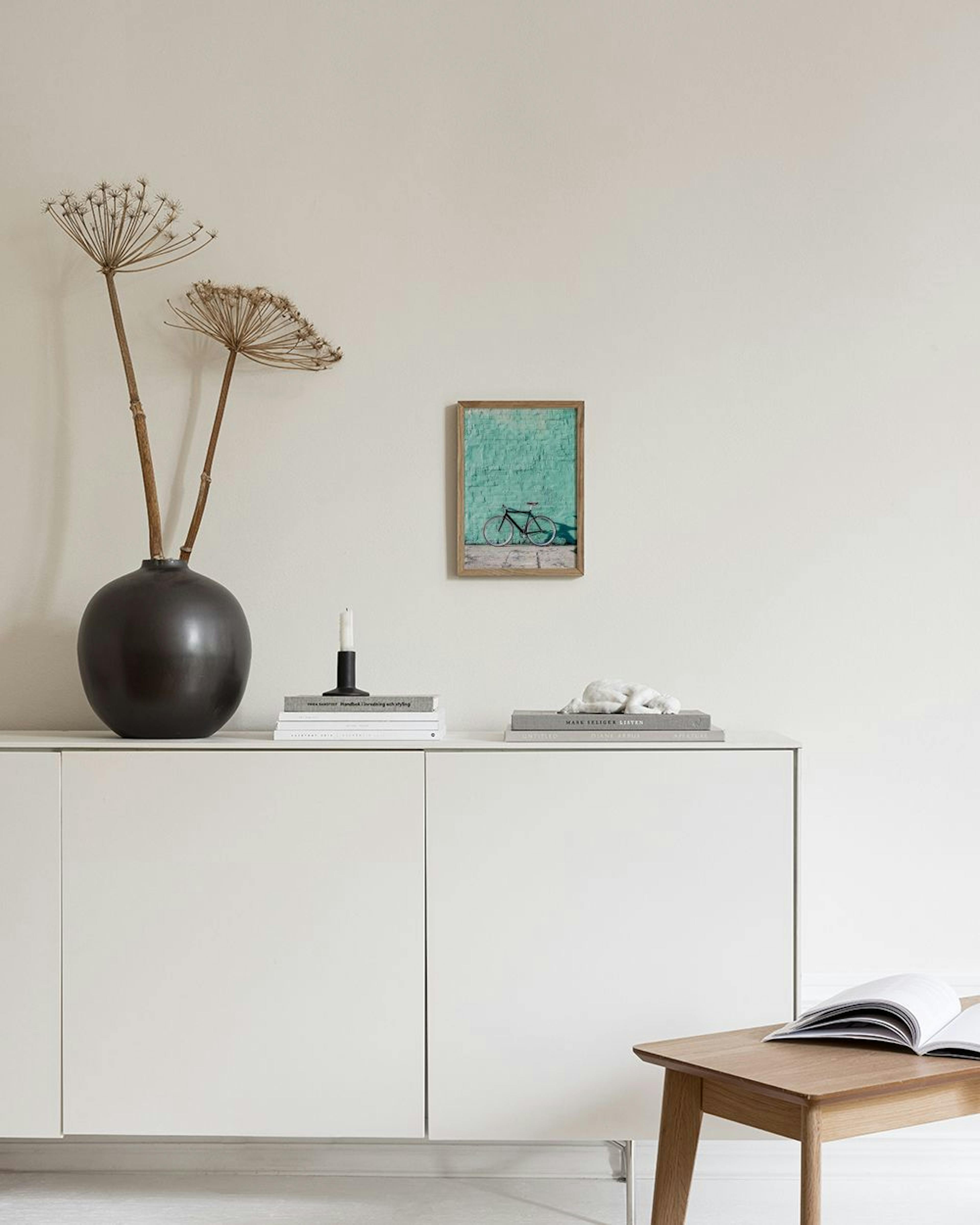 Een galeriewand met zes posters in mintgroen en roze, hangend in een moderne kamer boven een poef.