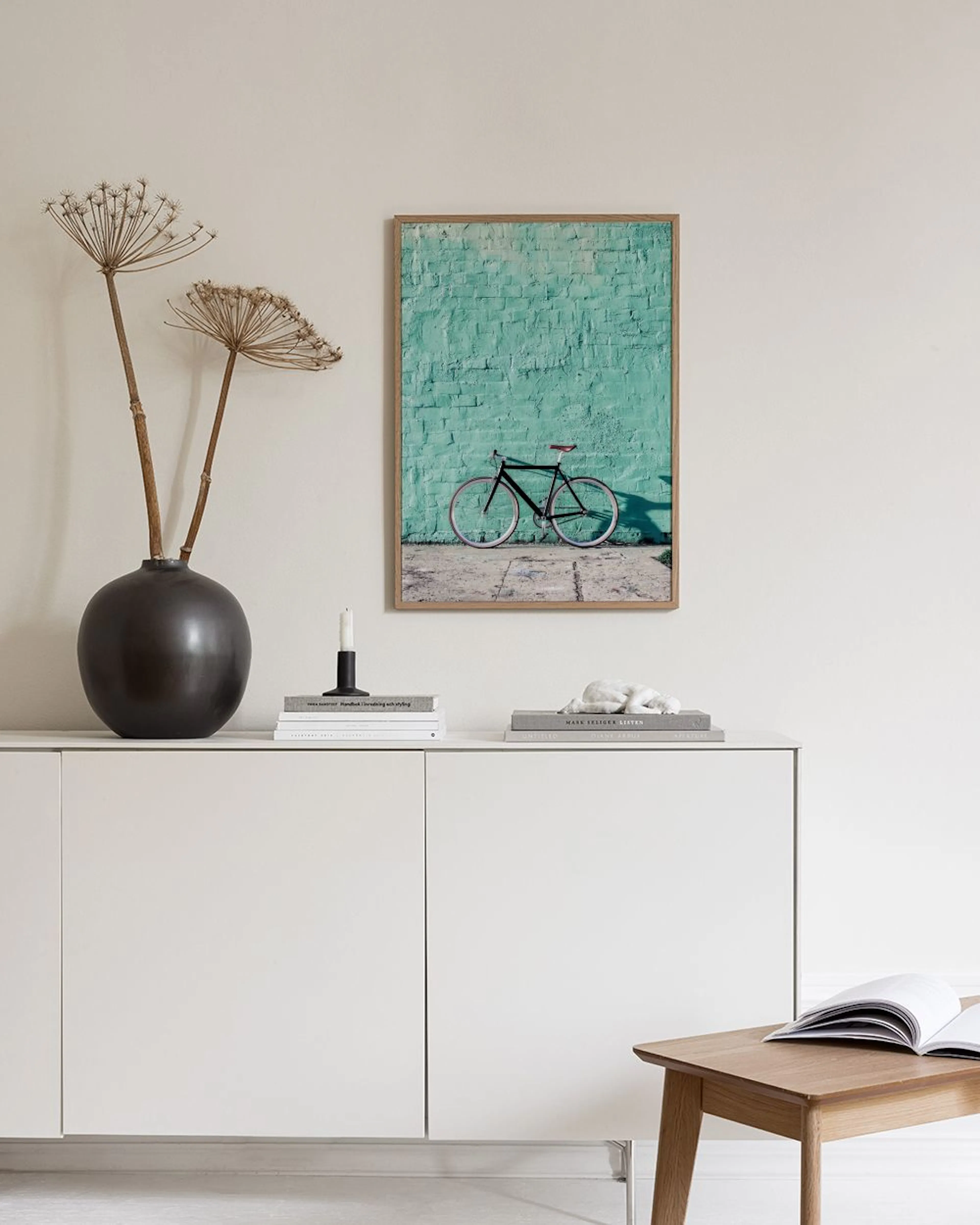 Sei poster con tonalità acquamarina, rosa e verde, appesi a una parete grigia sopra un pouf imbottito con cuscini.