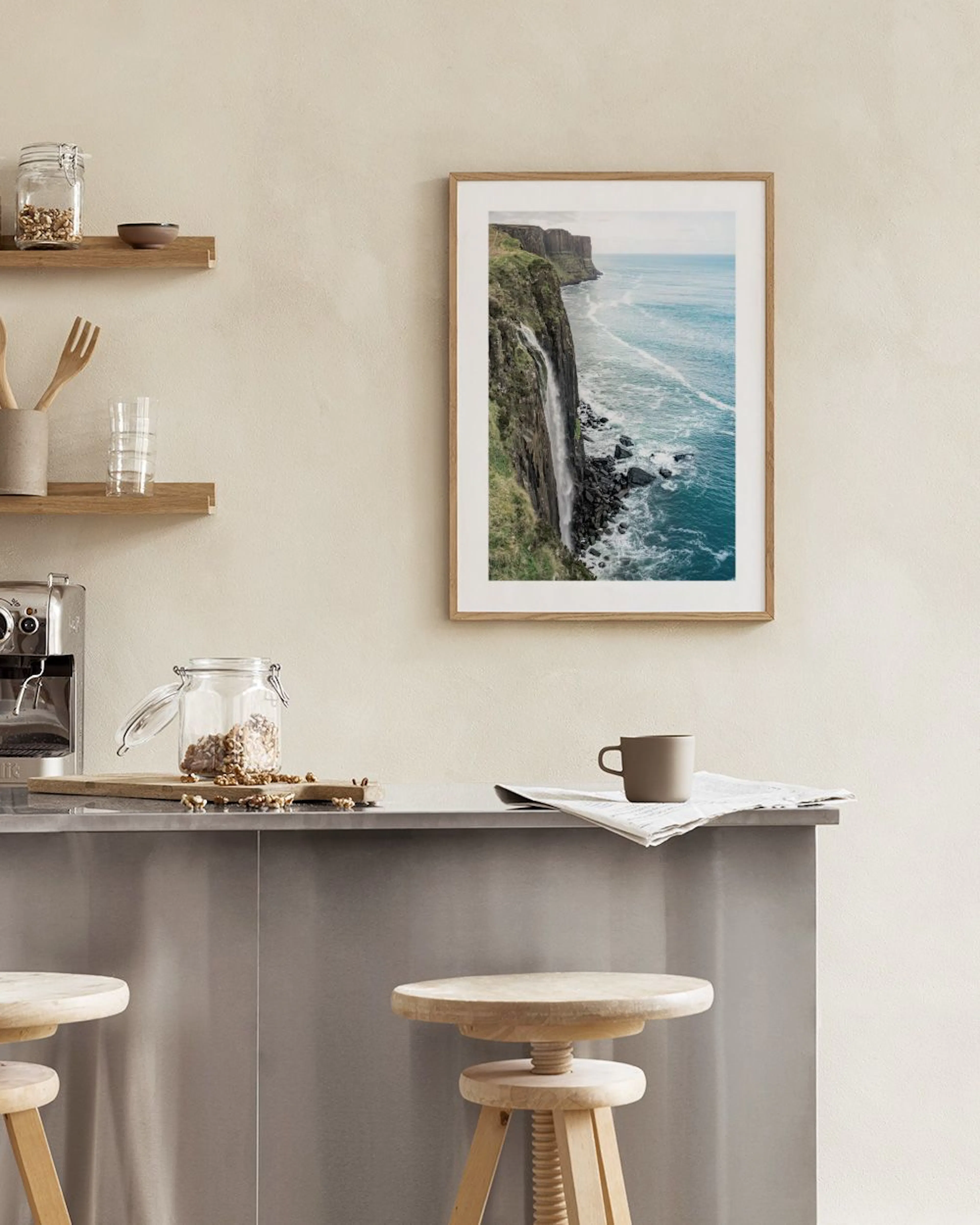A print of a dramatic waterfall cascading down a green cliff face into a blue ocean, displayed above a wooden desk.