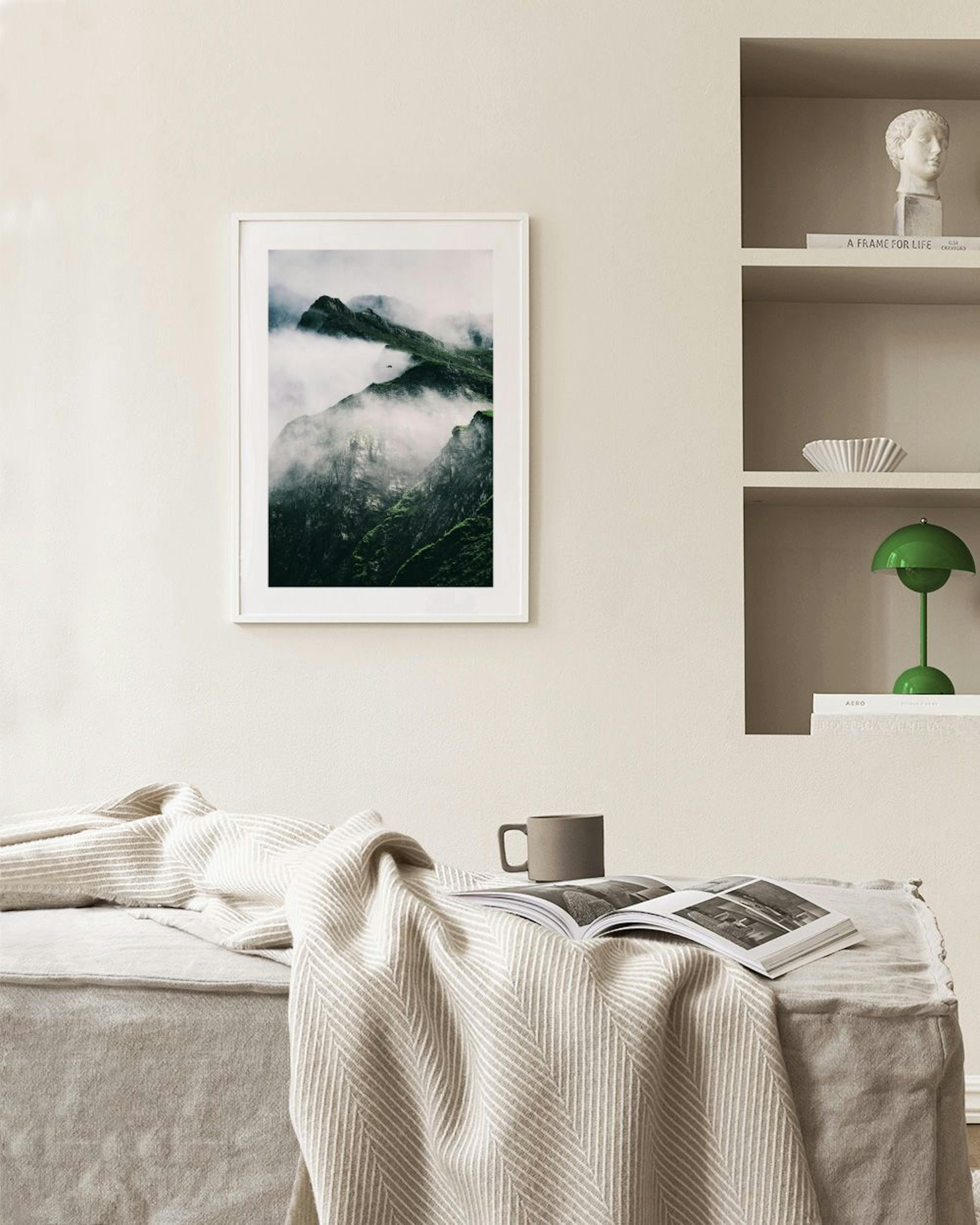 Affiche de montagnes suisses verdoyantes et brumeuses, suspendue au-dessus dun meuble blanc avec plante et vase.