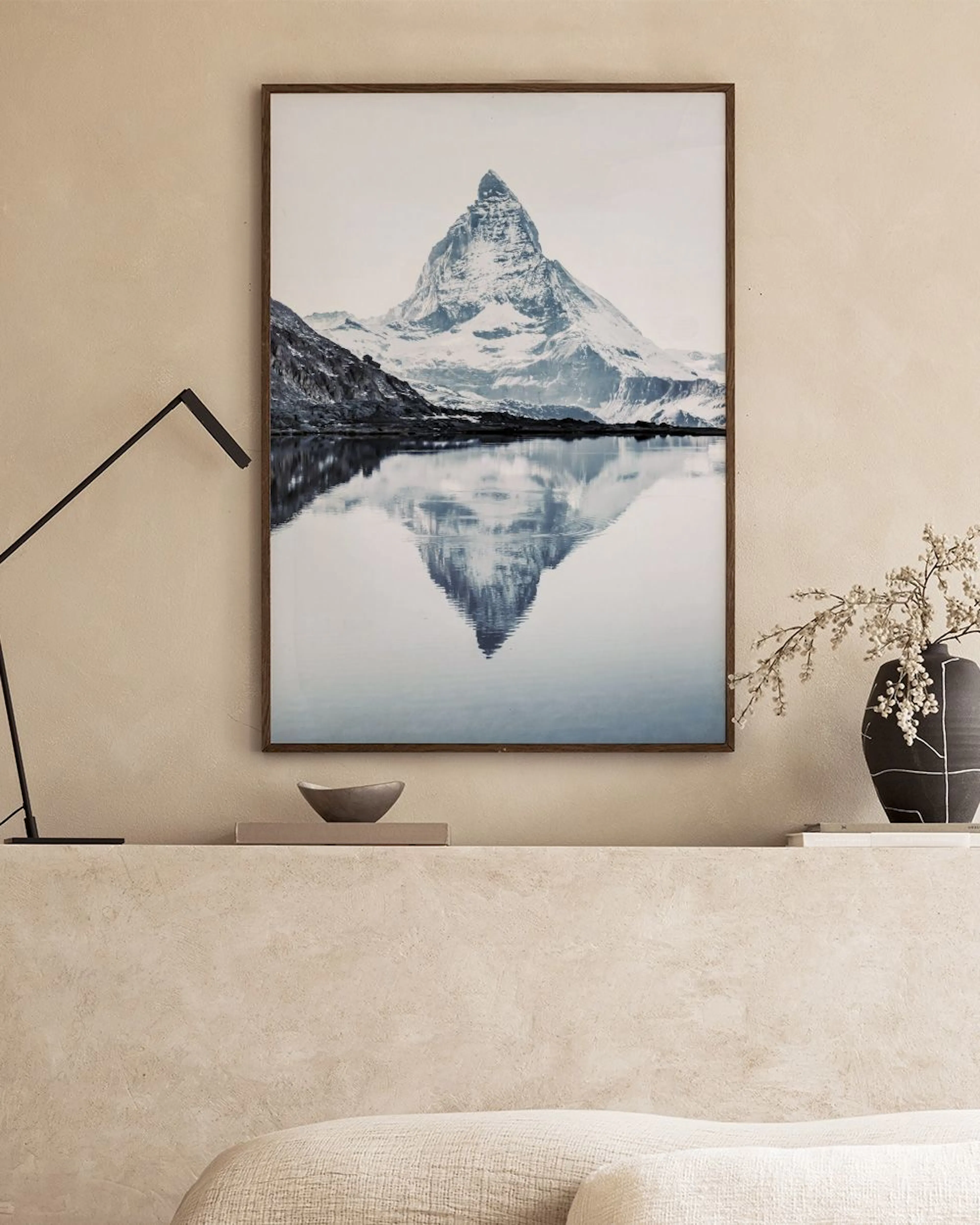 Poster van de besneeuwde Matterhorn weerspiegeld in een meer, hangend boven een houten bankje met plant en vazen.