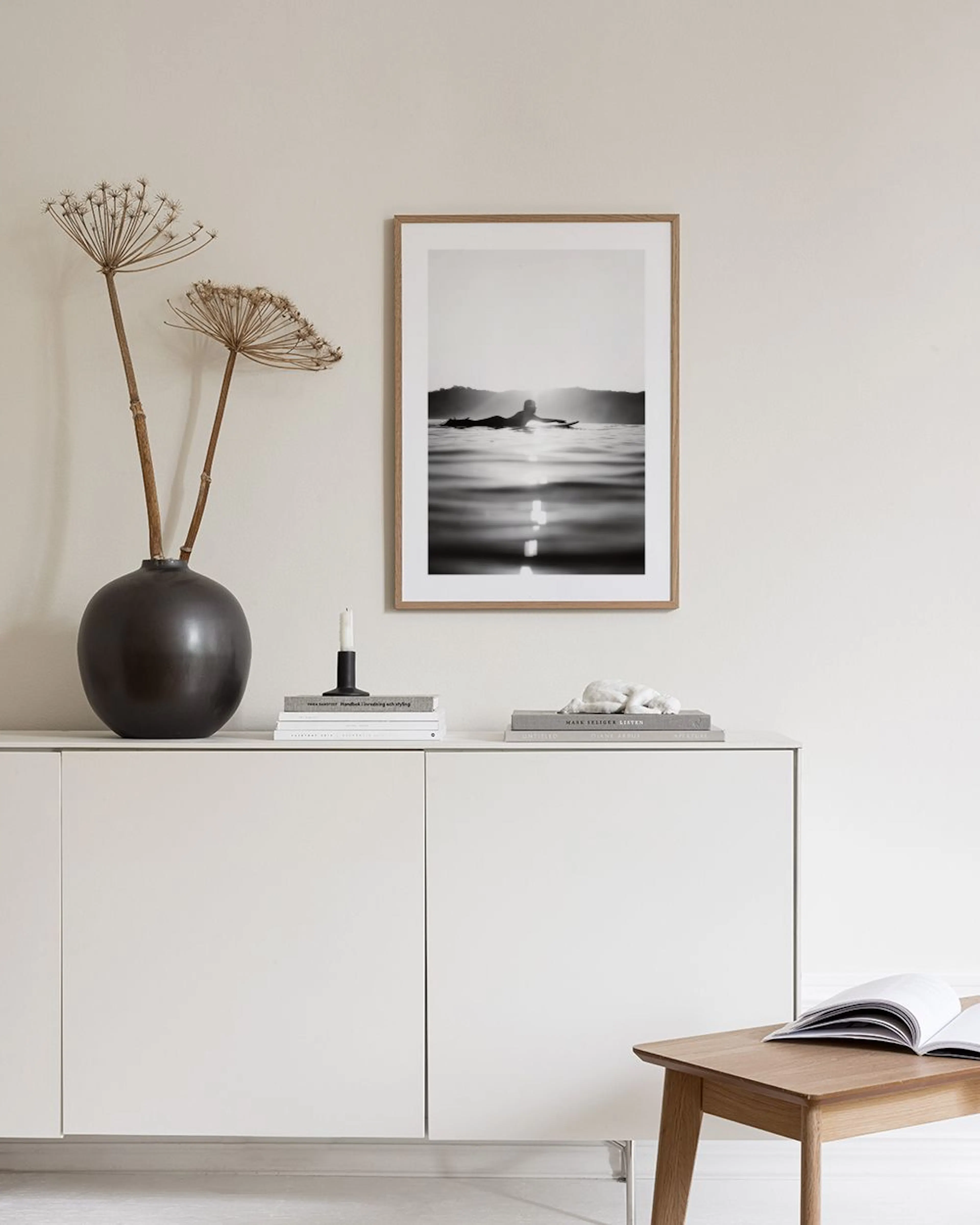 Affiche noir et blanc dun surfeur couché sur sa planche au coucher du soleil, accrochée au-dessus dun fauteuil taupe et dun cact