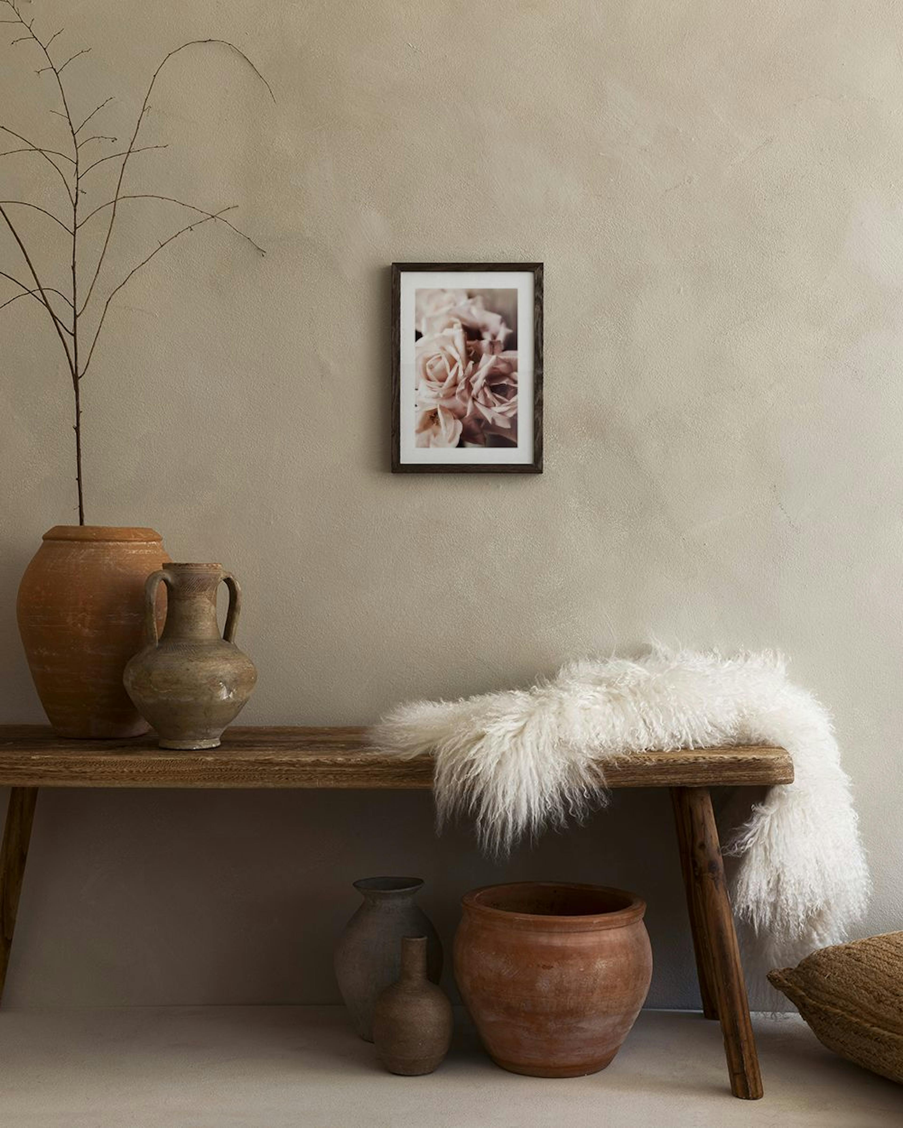 Poster med blekrosa rosor hängandes i ett sovrum ovanför ett sängbord med lampa och böcker.