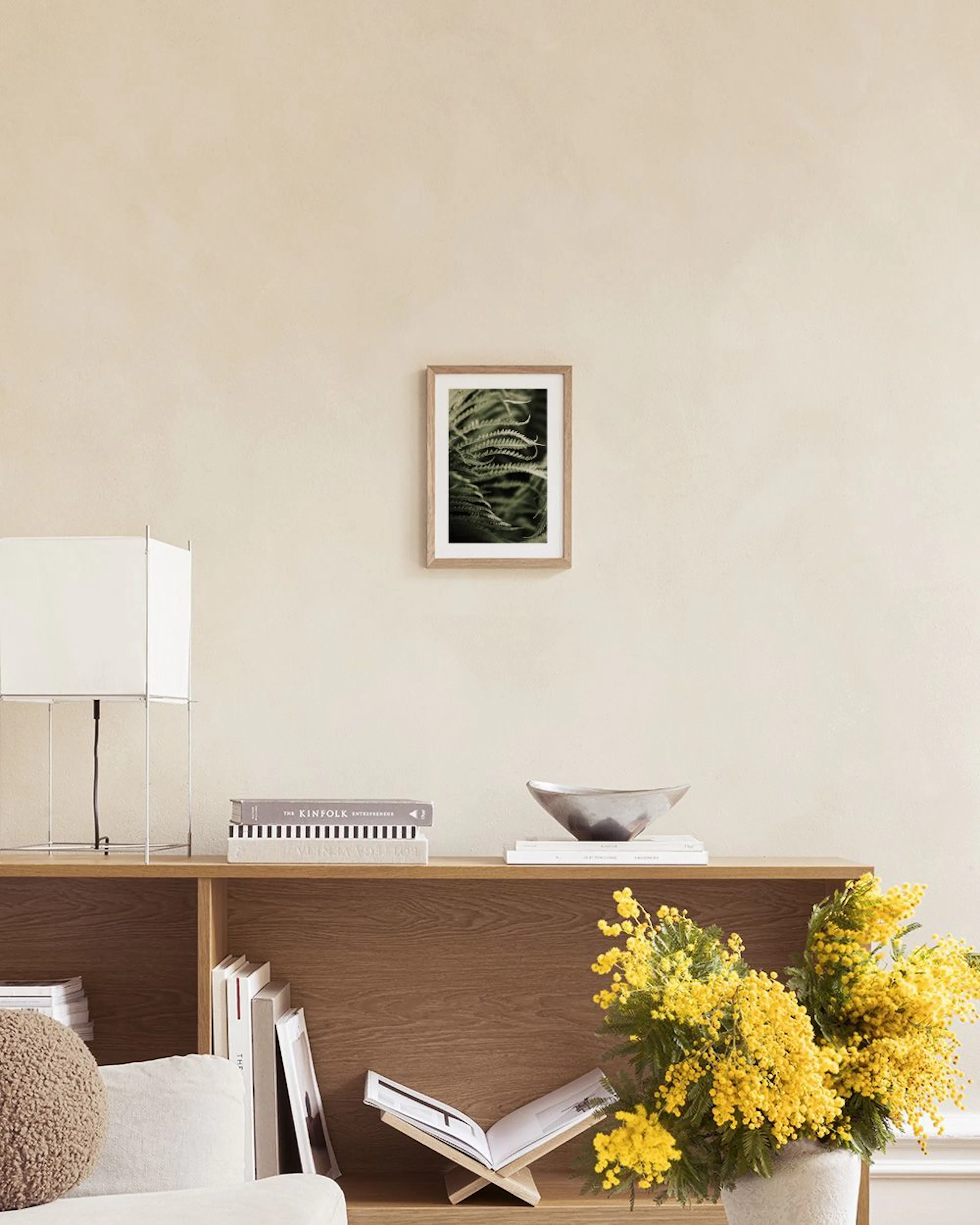 Affiche photo dune fougère verte luxuriante, suspendue au-dessus dune table basse avec vase et livres.