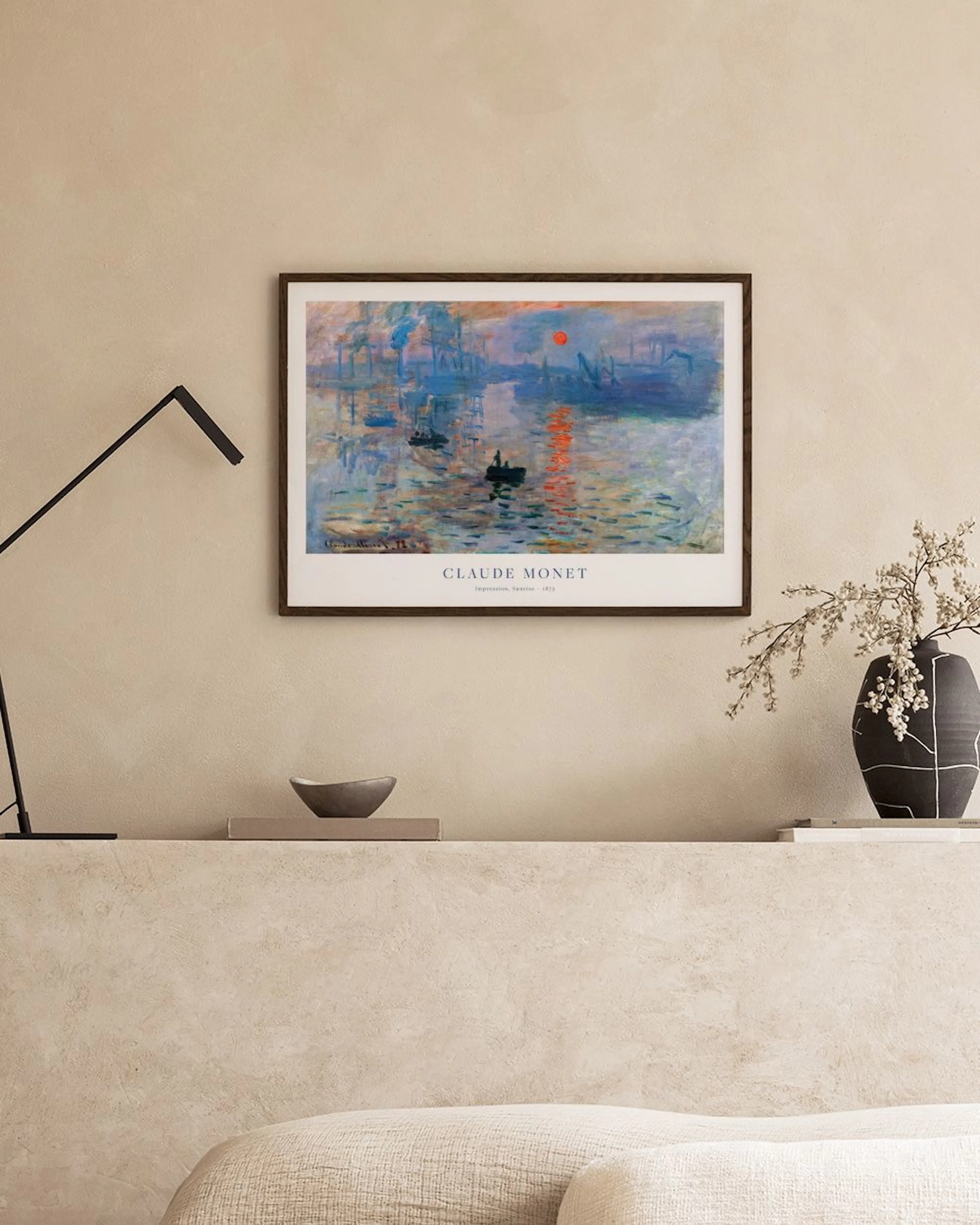 Póster de Impresión, sol naciente de Monet, con barcas y reflejos naranjas y azules, colgado sobre una mesa de madera.