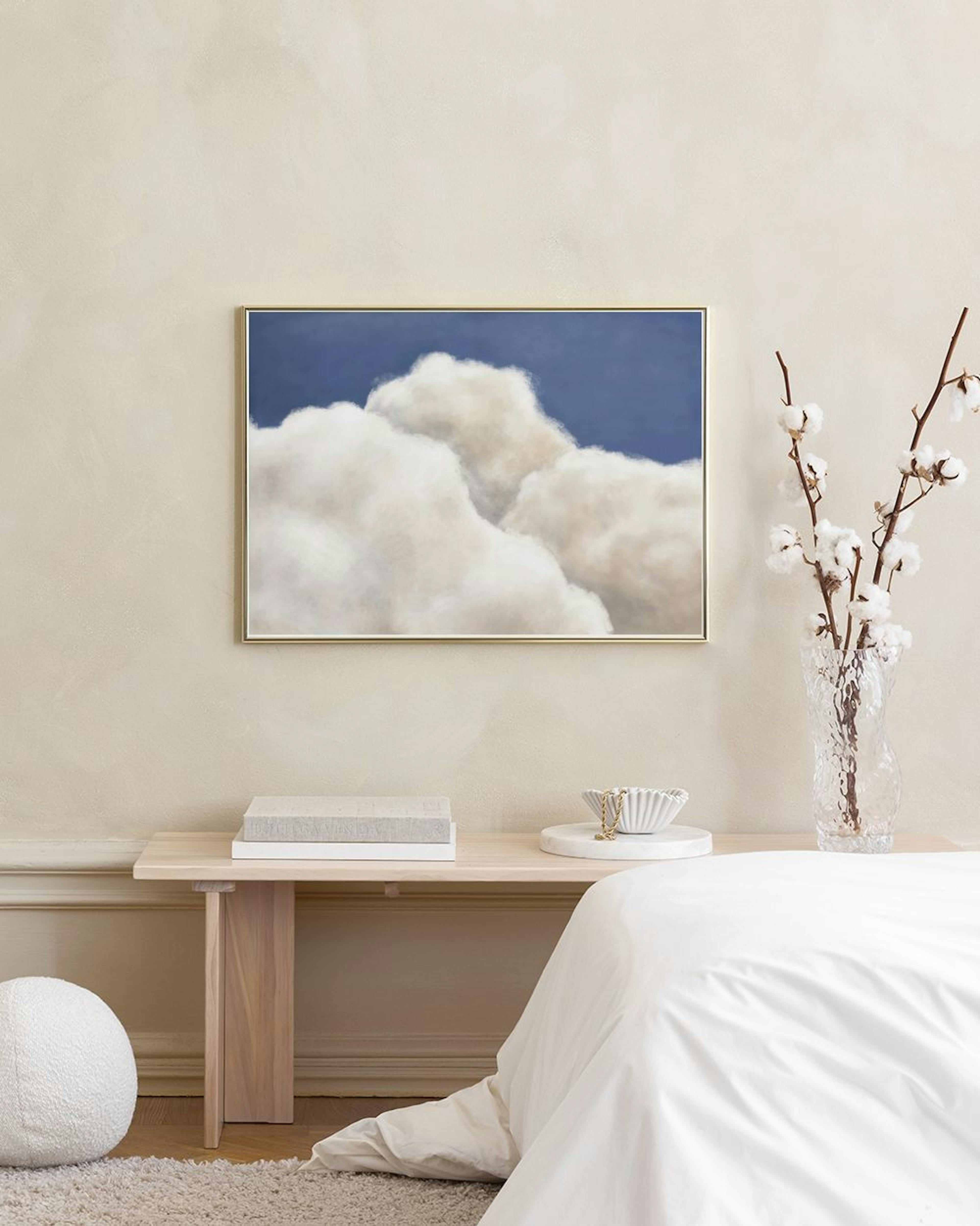 Póster de nubes blancas y esponjosas sobre un cielo azul, colgado sobre una mesa de madera con vasos y un banco.