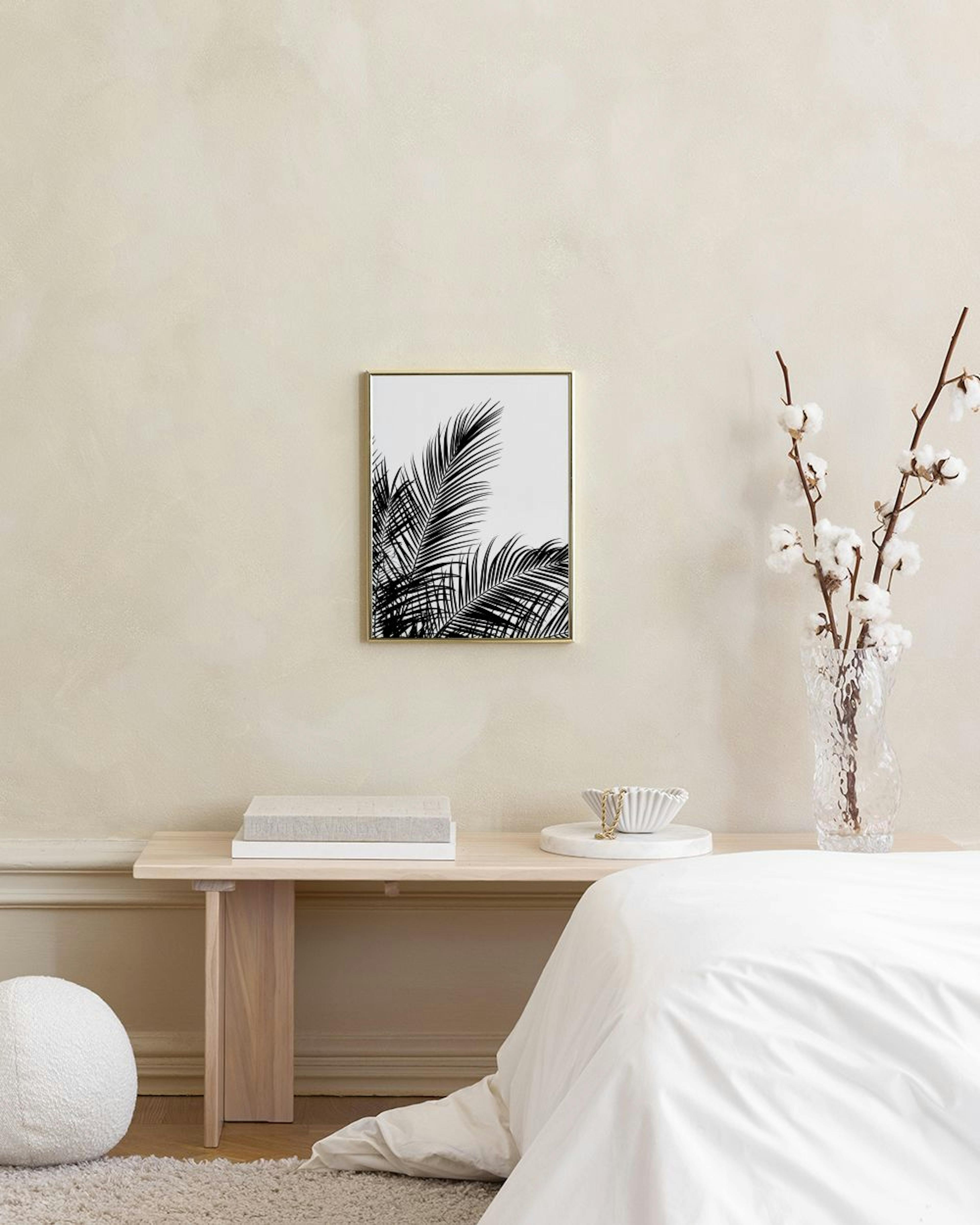 Póster de hojas de palmera en blanco y negro, colgado sobre un taburete con libros en una habitación luminosa.