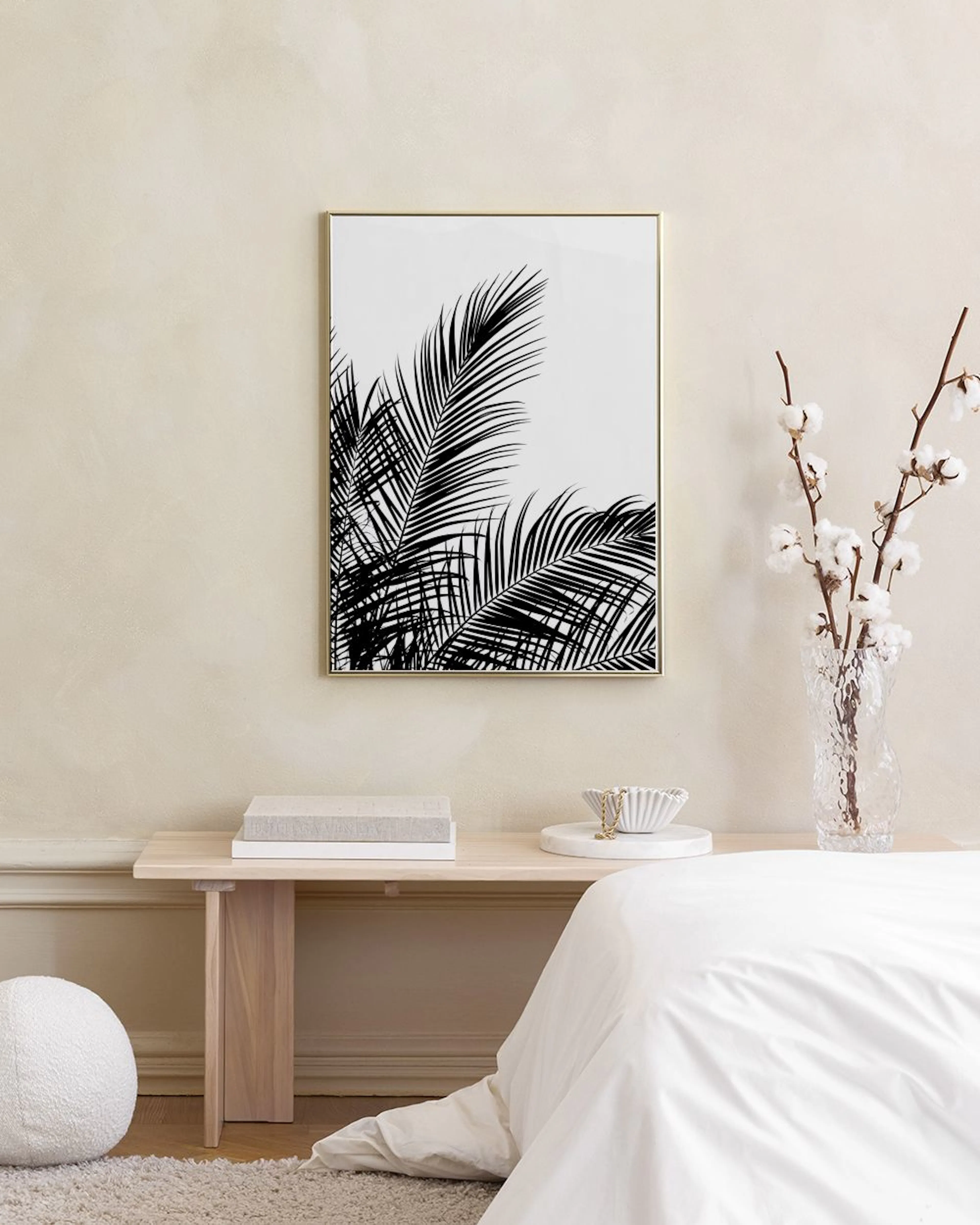 A black and white palm print hanging above a cork stool with books, in a room with white walls and wood floor.