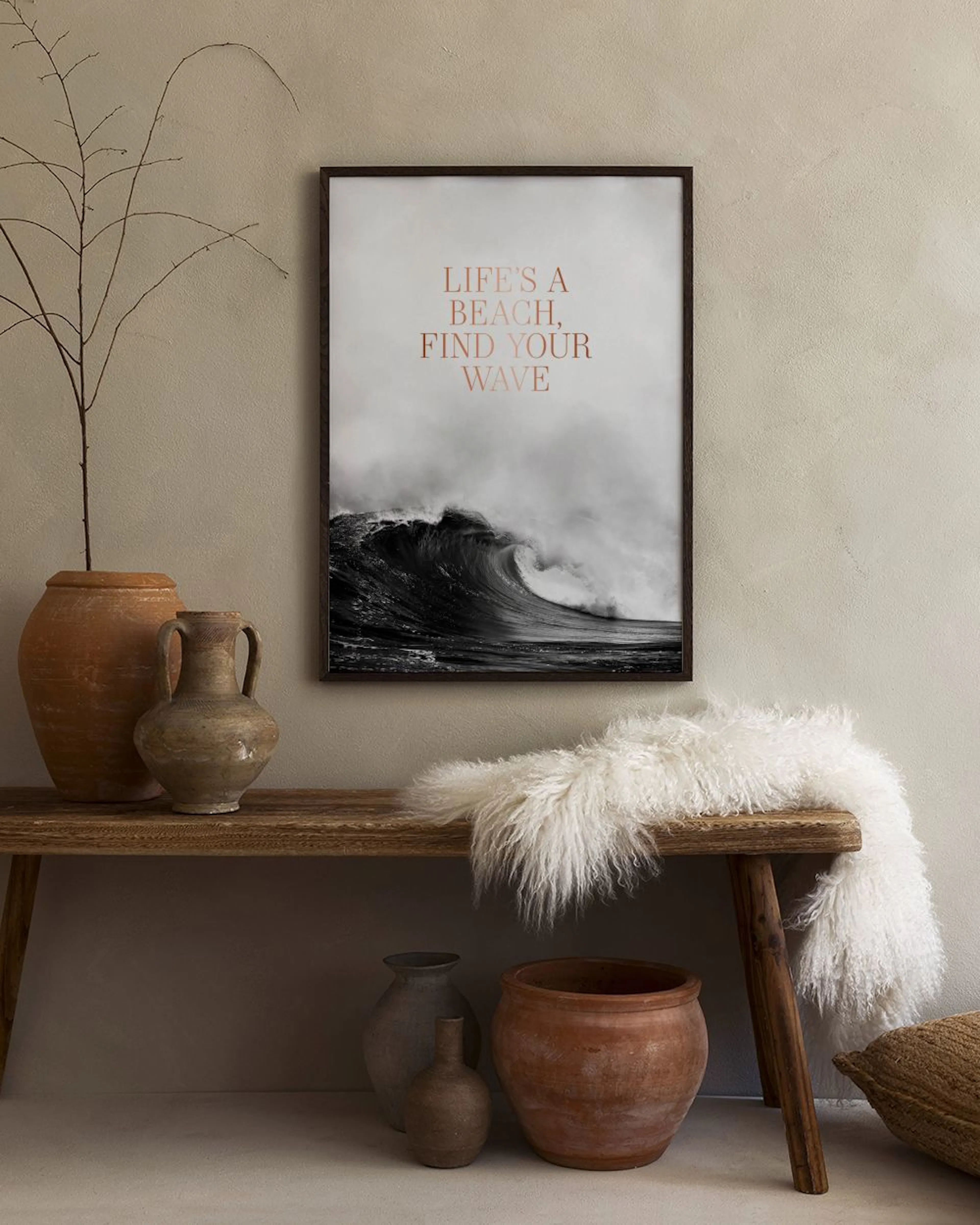 Plakat z czarno-białą falą i napisem Lifes a beach, find your wave, wiszący na szarej ścianie nad czarnymi stolikami.