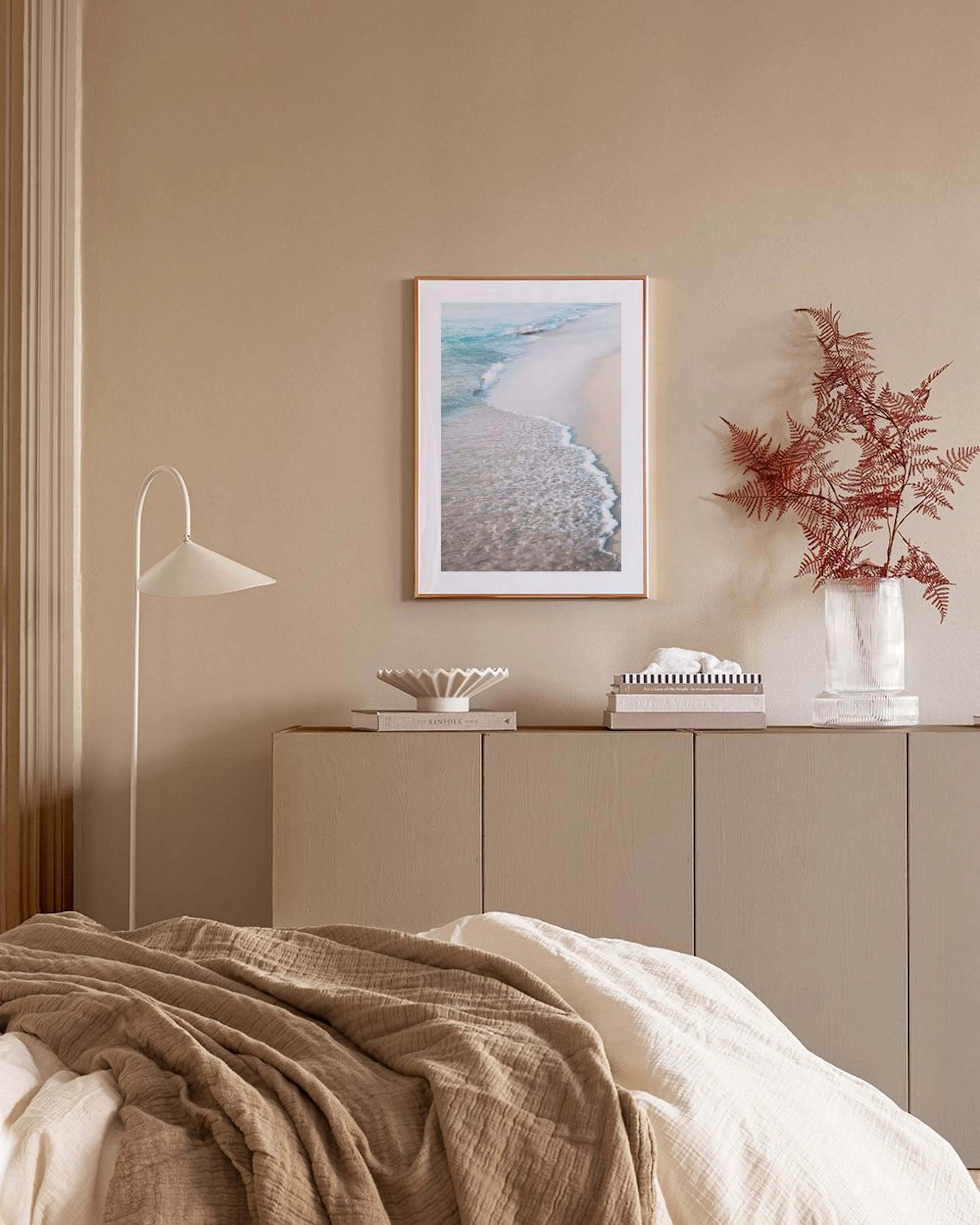Poster de uma praia com ondas sobre uma bancada creme, com dois vasos e livros.