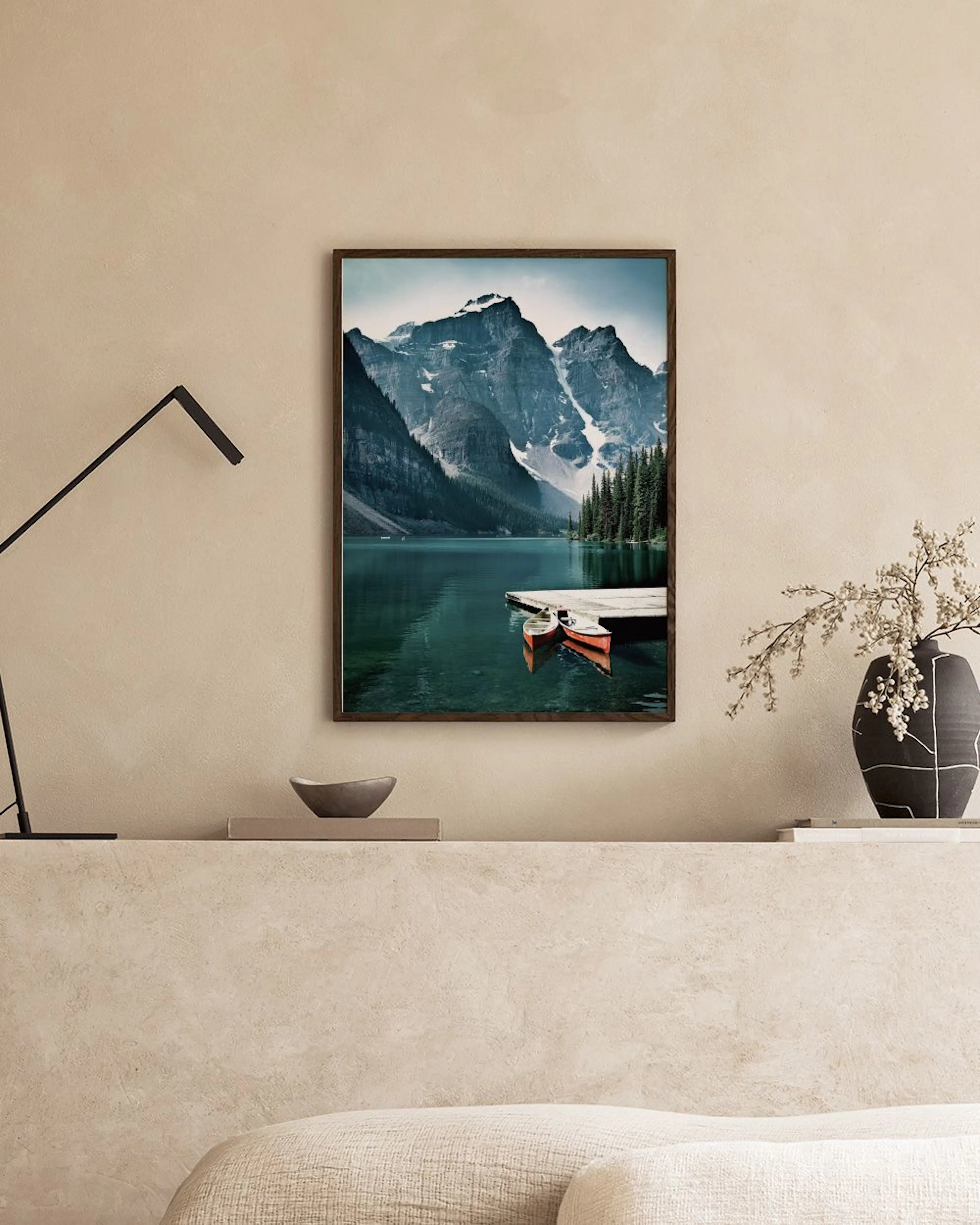 Póster de un lago de montaña con pinos y dos canoas junto a un muelle, colgado sobre un sillón verde.