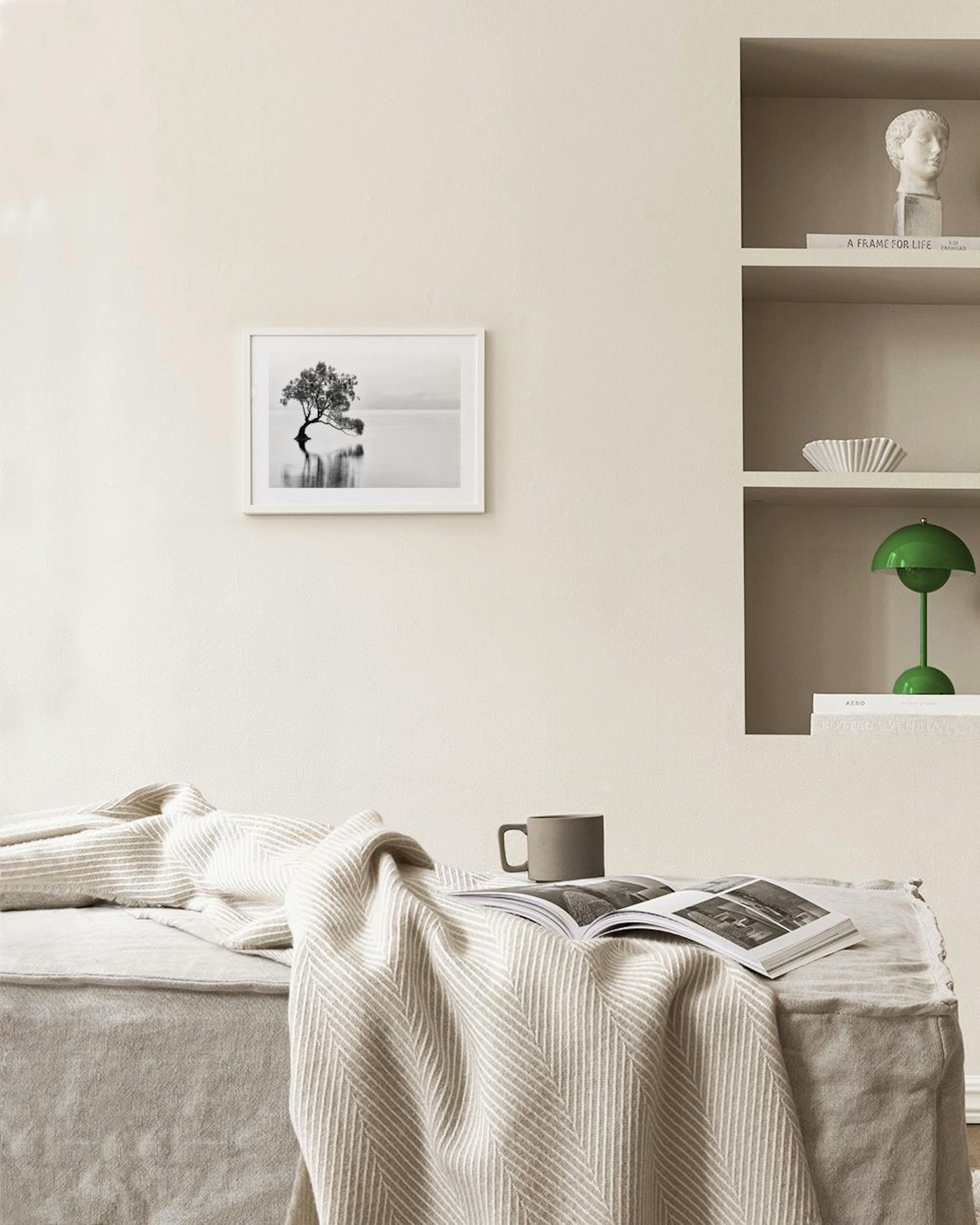 Póster de árbol solitario en agua, en blanco y negro, colgado sobre un sillón verde en una sala moderna.