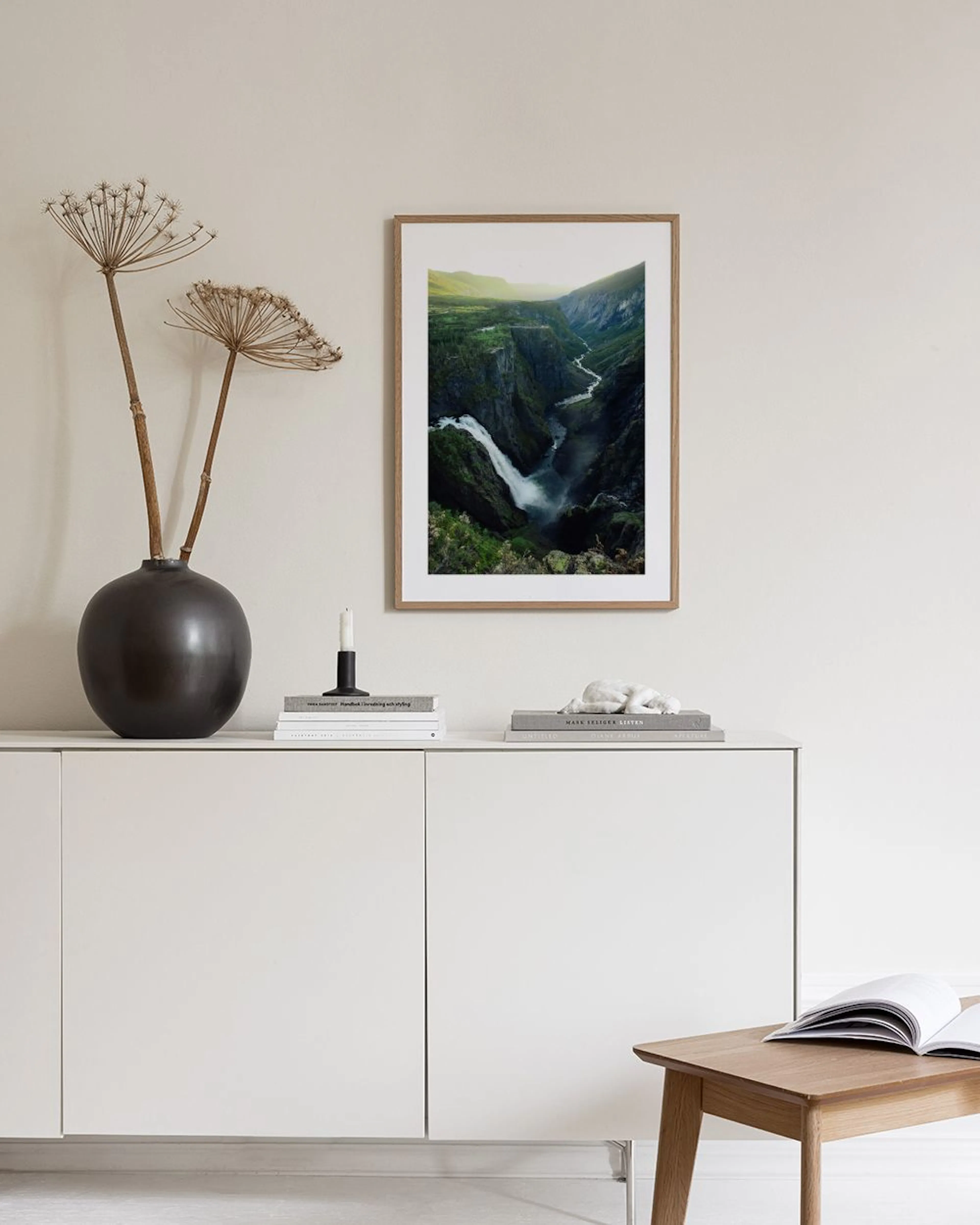 Affiche de cascade dans un canyon verdoyant, accrochée au-dessus dun meuble blanc avec un vase rond, à côté dune porte.