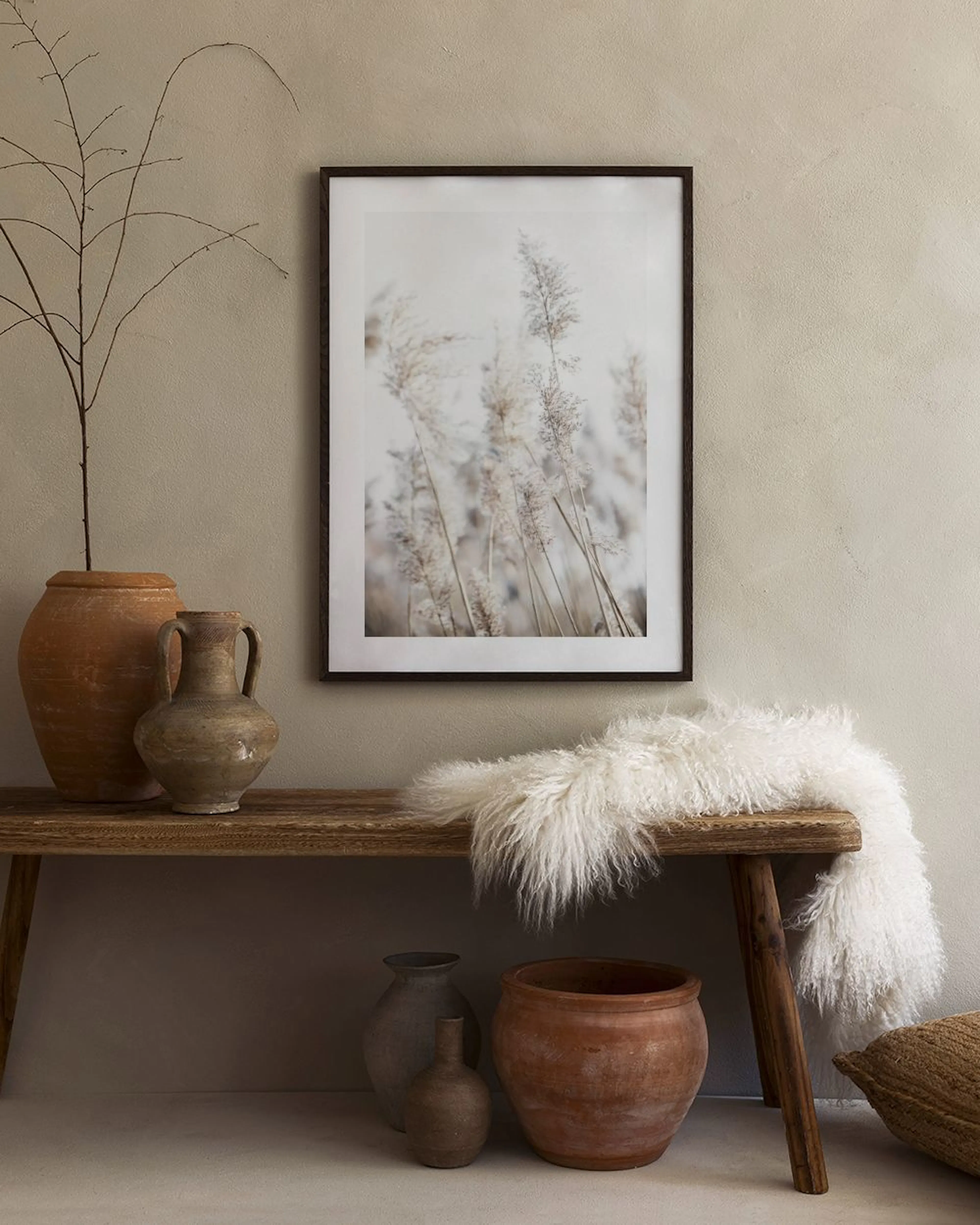 A print of dry pampas grass in light brown and beige tones, hanging on a gray wall above a beige armchair.