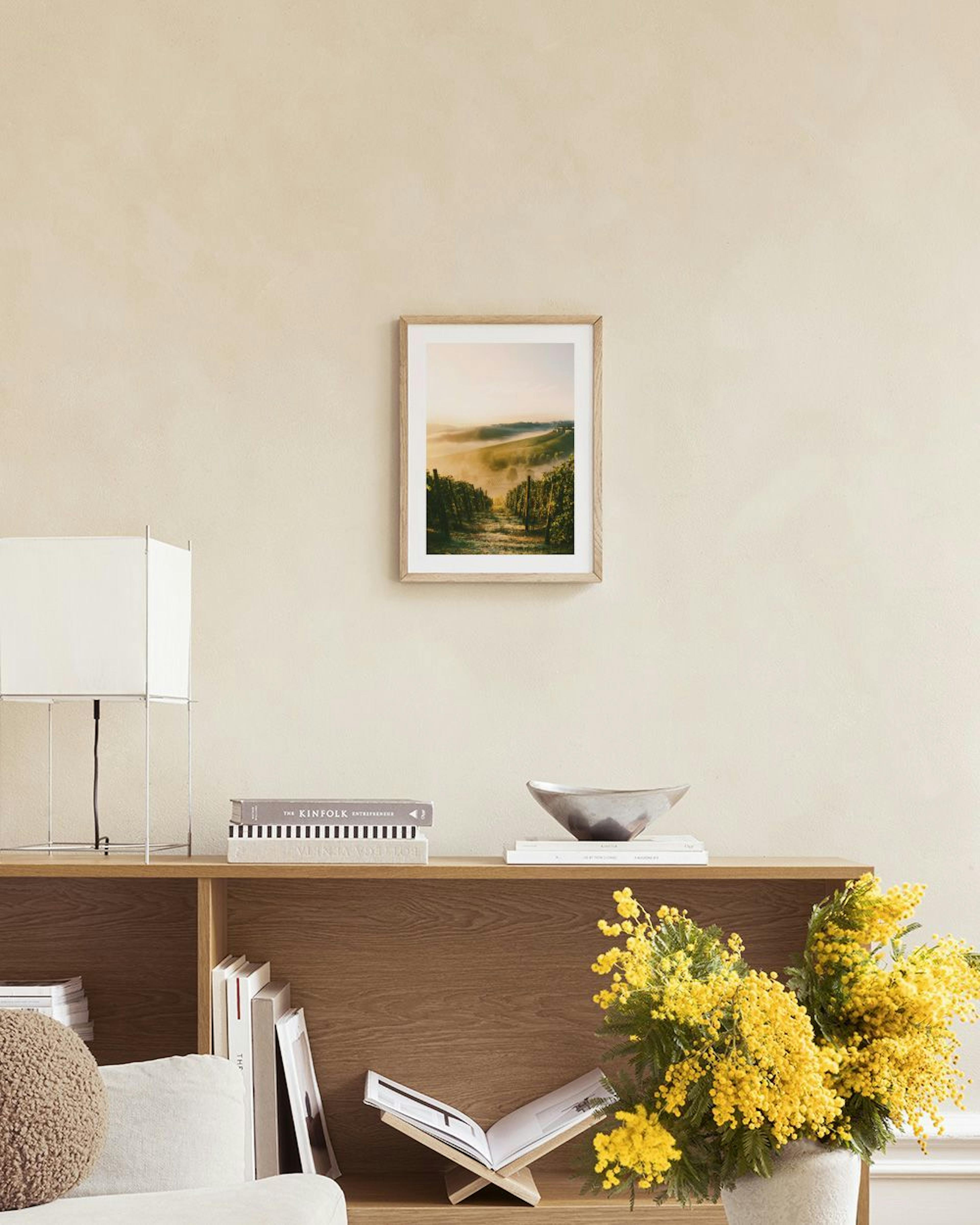 Poster eines sonnigen Weinbergs im Nebel, hängt über einem Sideboard mit Vasen und Büchern.