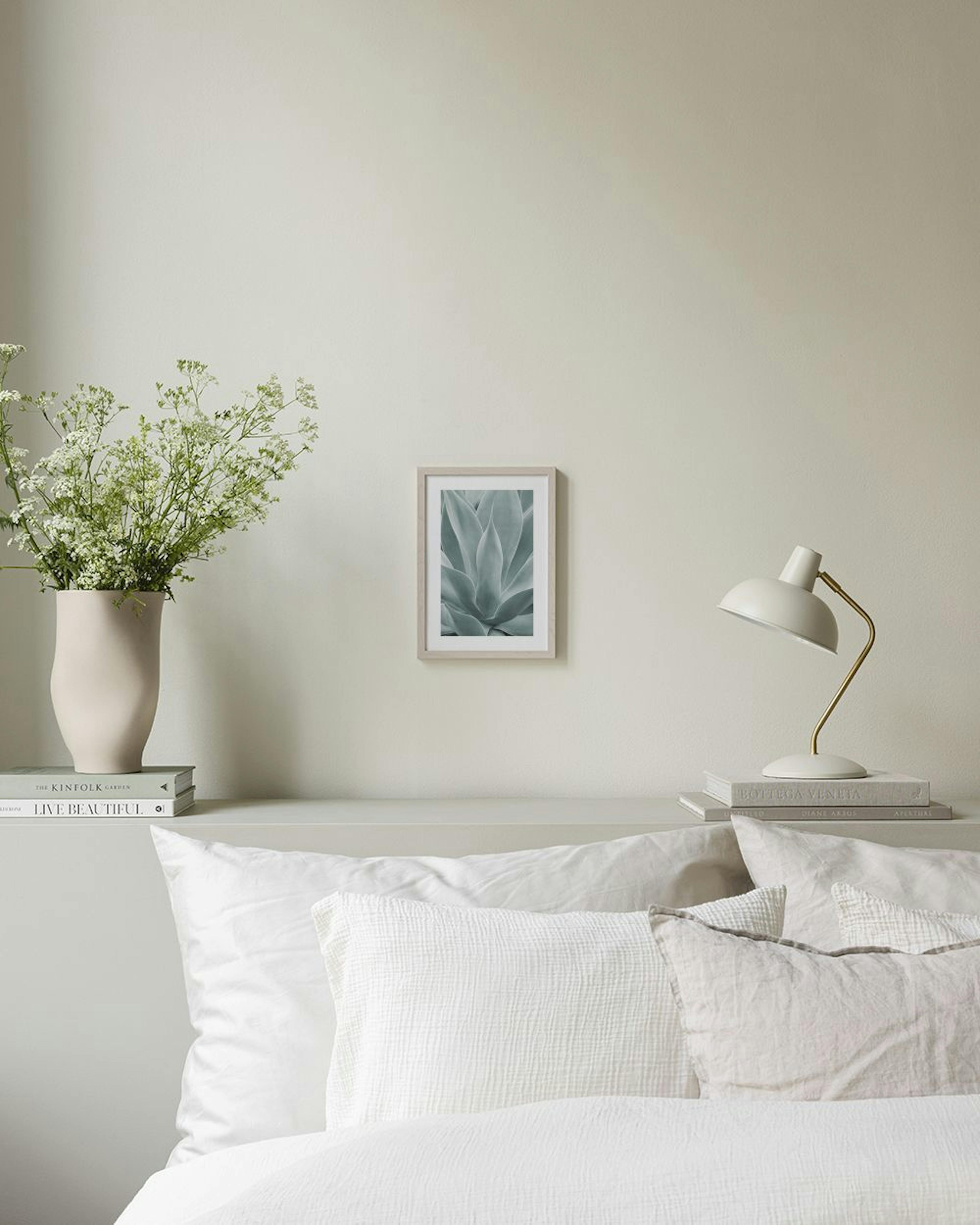Poster de planta suculenta verde-cinzenta com folhas largas, pendurado numa parede branca, com um vaso cinzento numa mesa e uma 