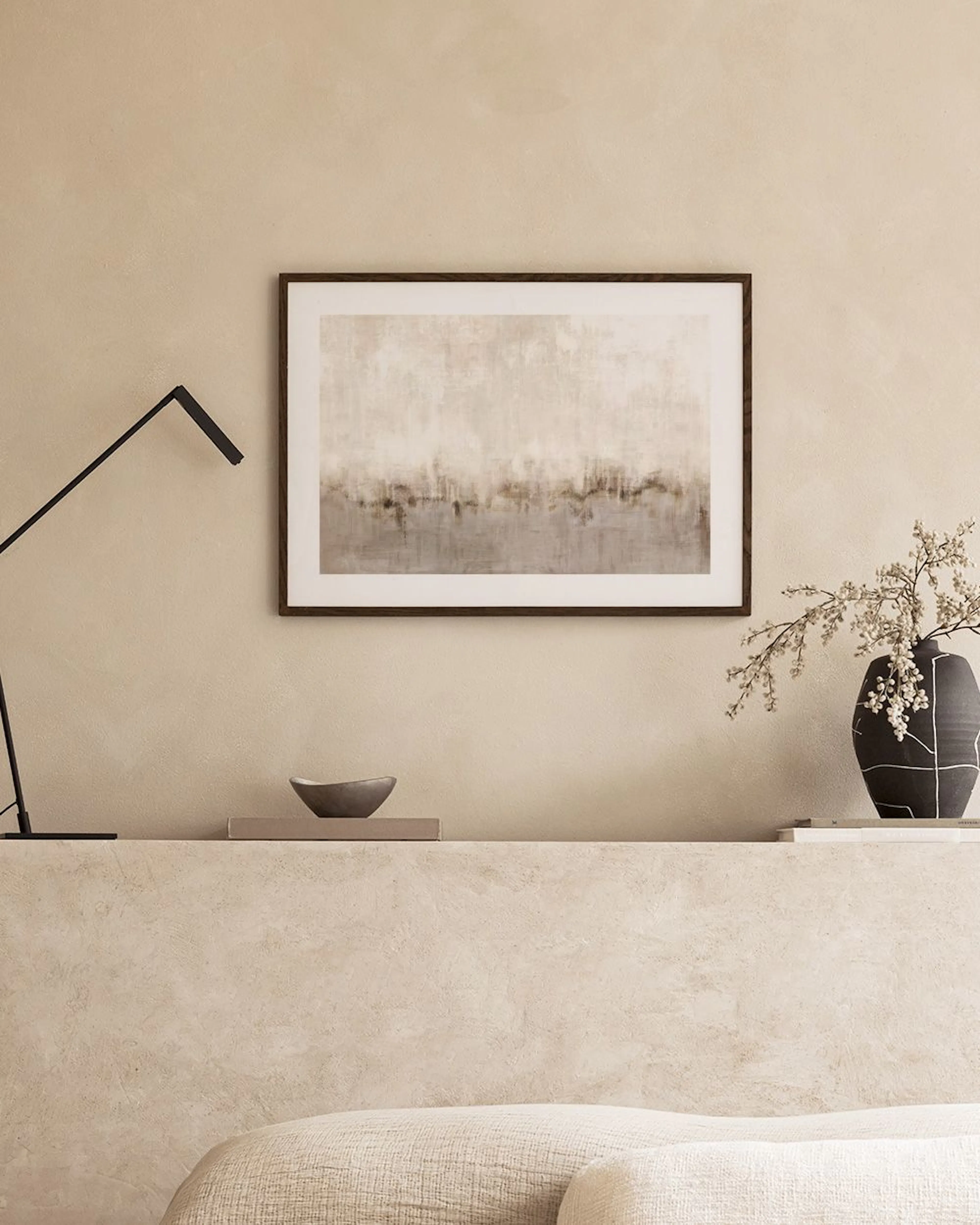 Abstract print with earthy tones of beige and brown, resembling a textured landscape, hanging above a grey coffee table and a ve