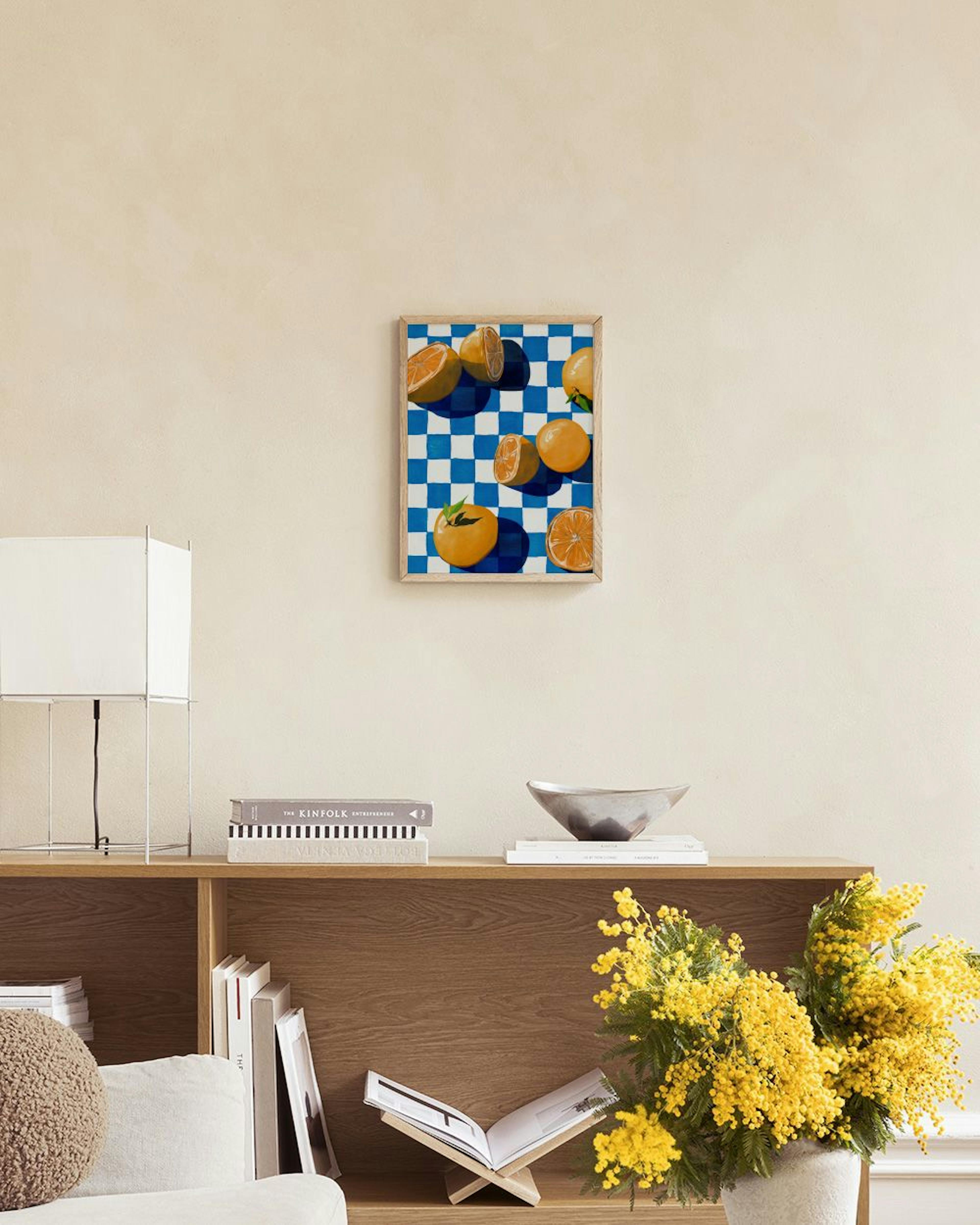 Poster de laranjas inteiras e cortadas sobre um fundo xadrez azul e branco, pendurado numa sala de estar moderna.